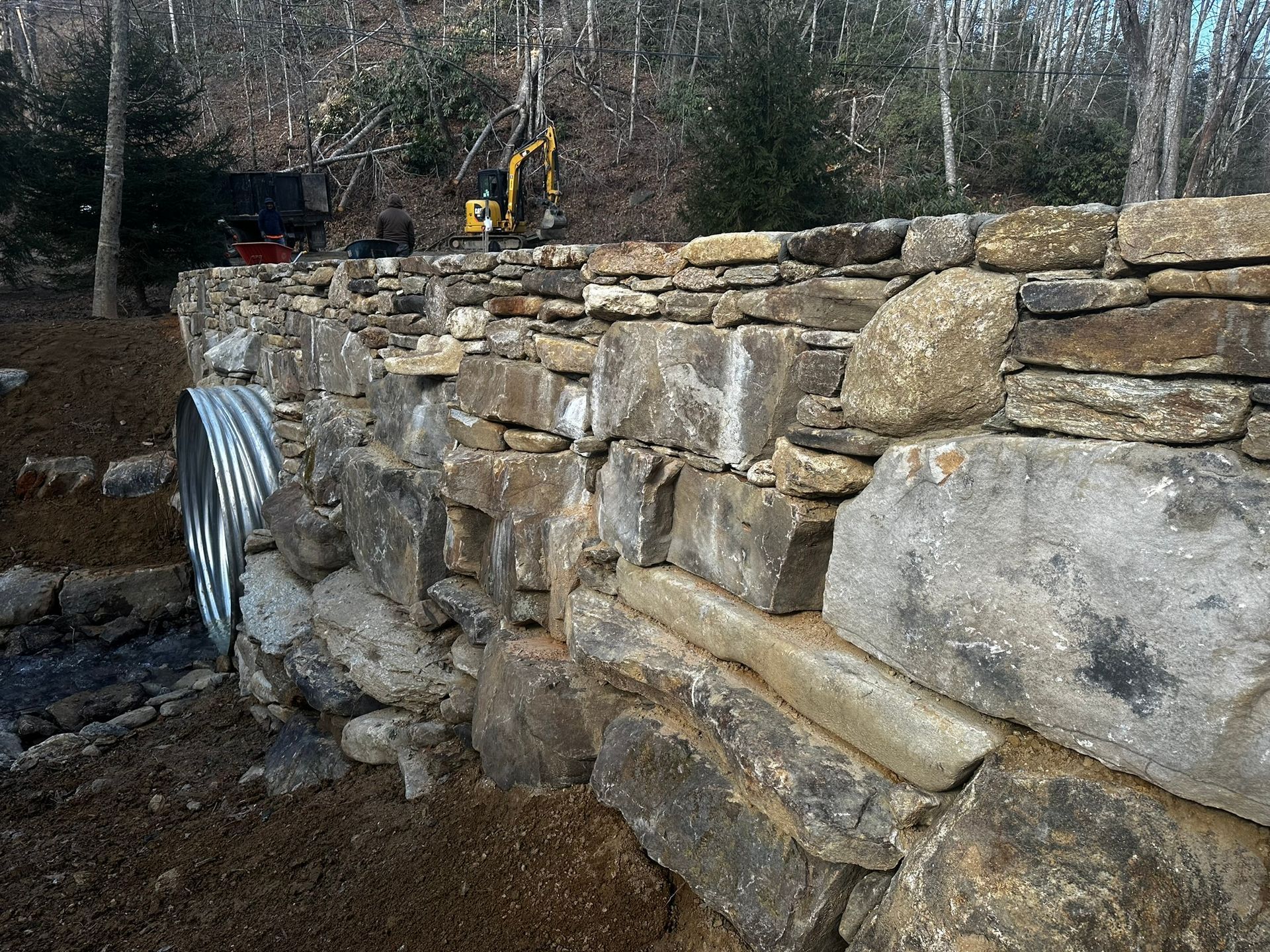 A large stone wall is being built in the woods.