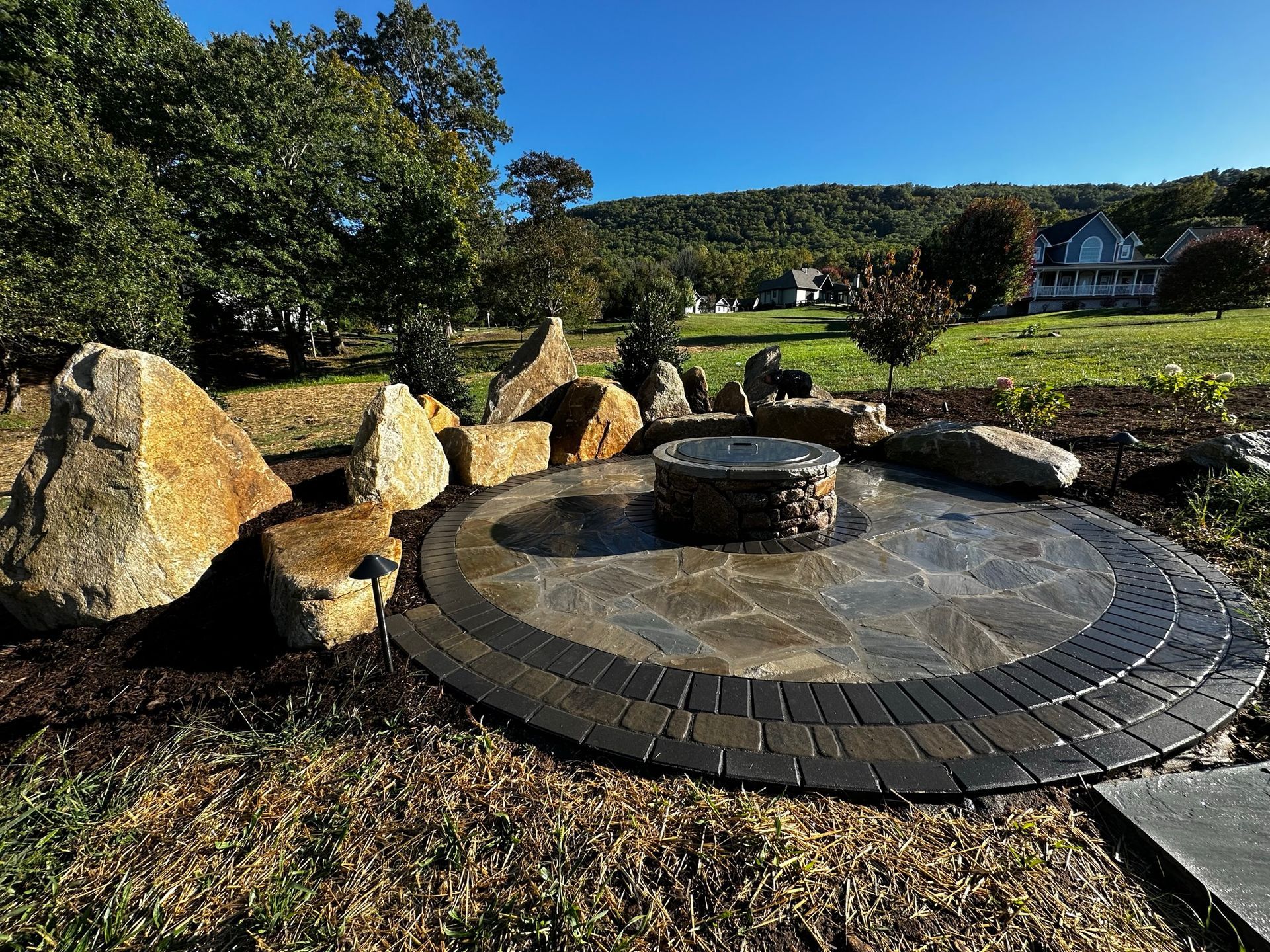A fire pit is surrounded by rocks and bricks in a backyard.