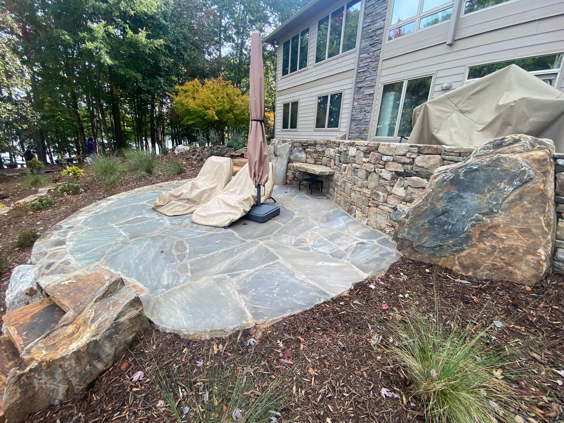 A stone patio with a umbrella and chairs in front of a house.