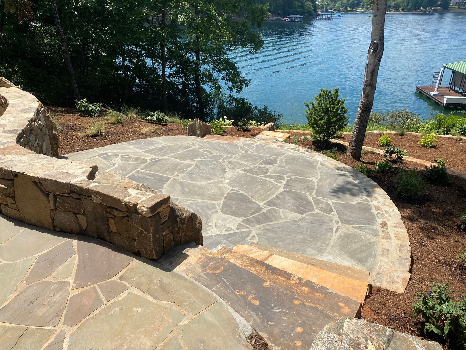 A stone patio overlooking a lake with a dock in the background.