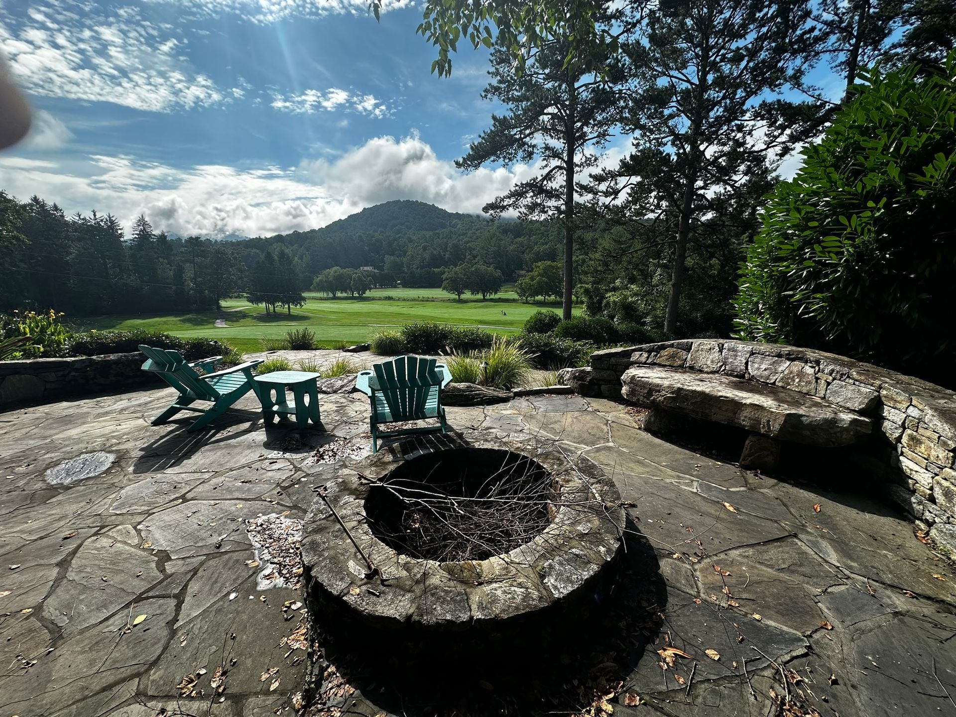 A stone patio with a fire pit and chairs with a view of a golf course.