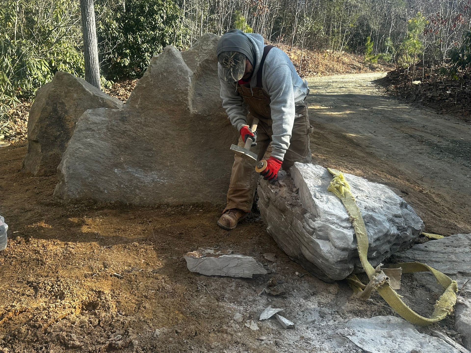 A man is working on a large rock in the dirt.