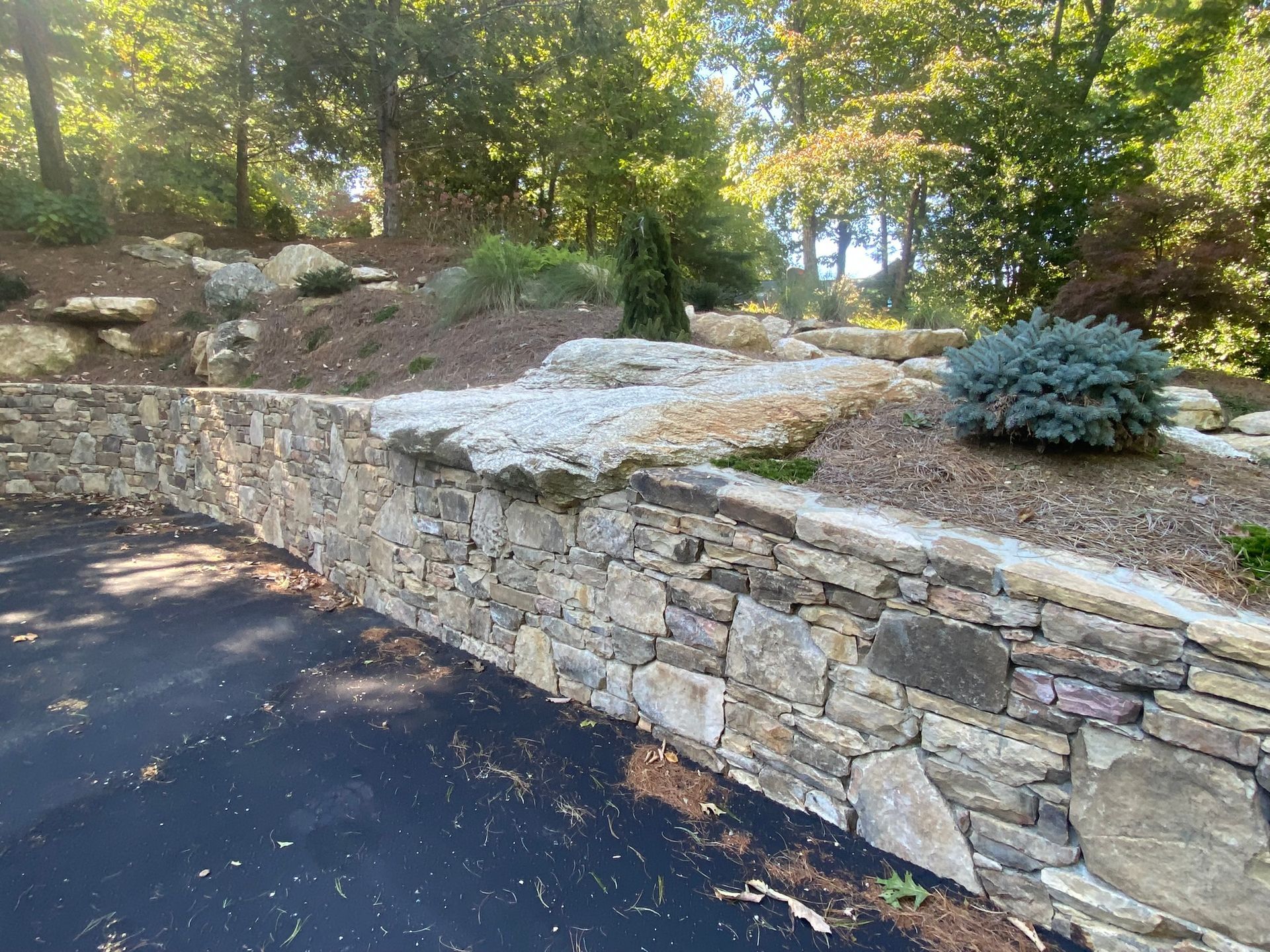 A stone wall surrounds a driveway with trees in the background.