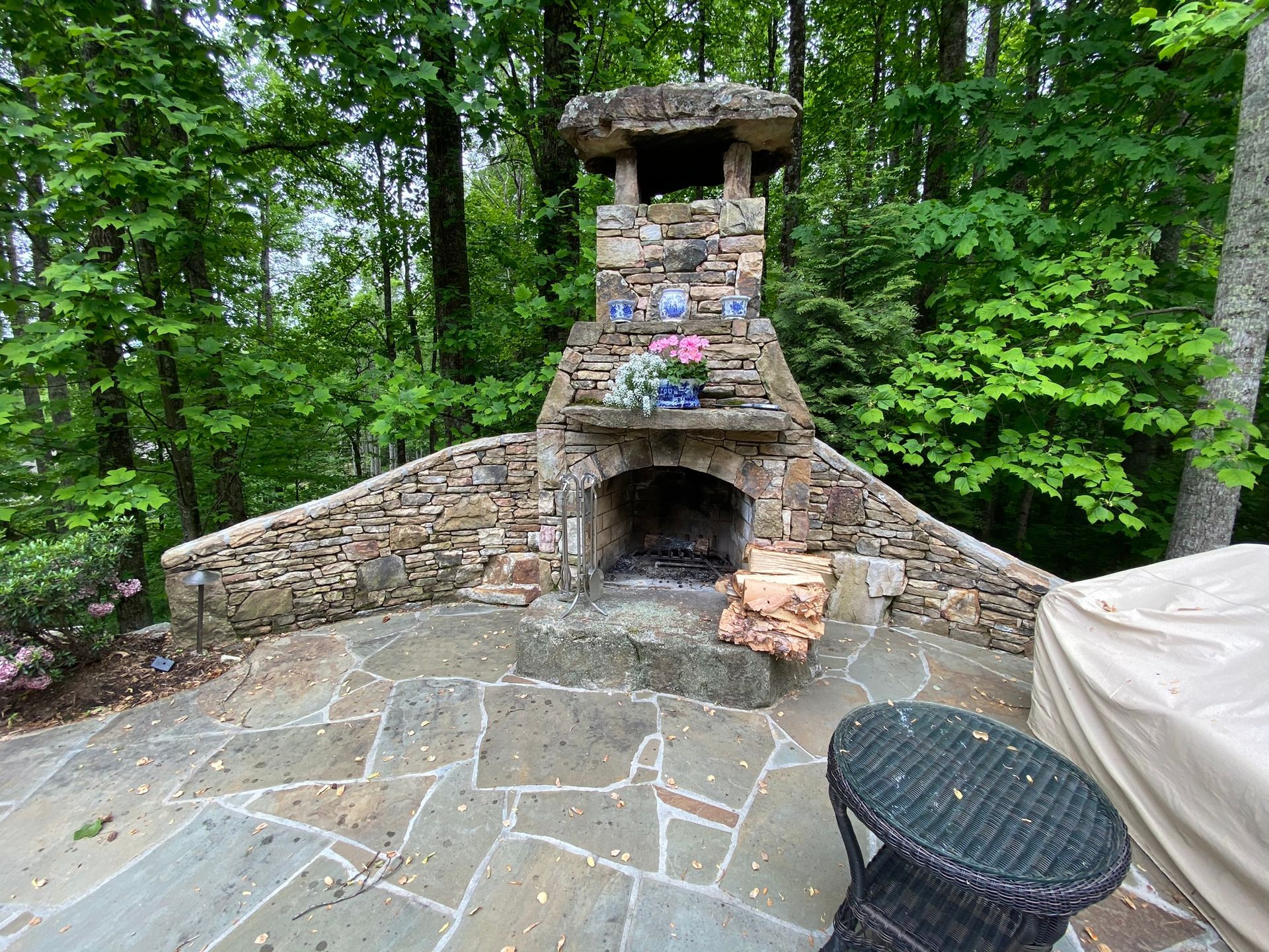 A stone fireplace is surrounded by trees on a patio.