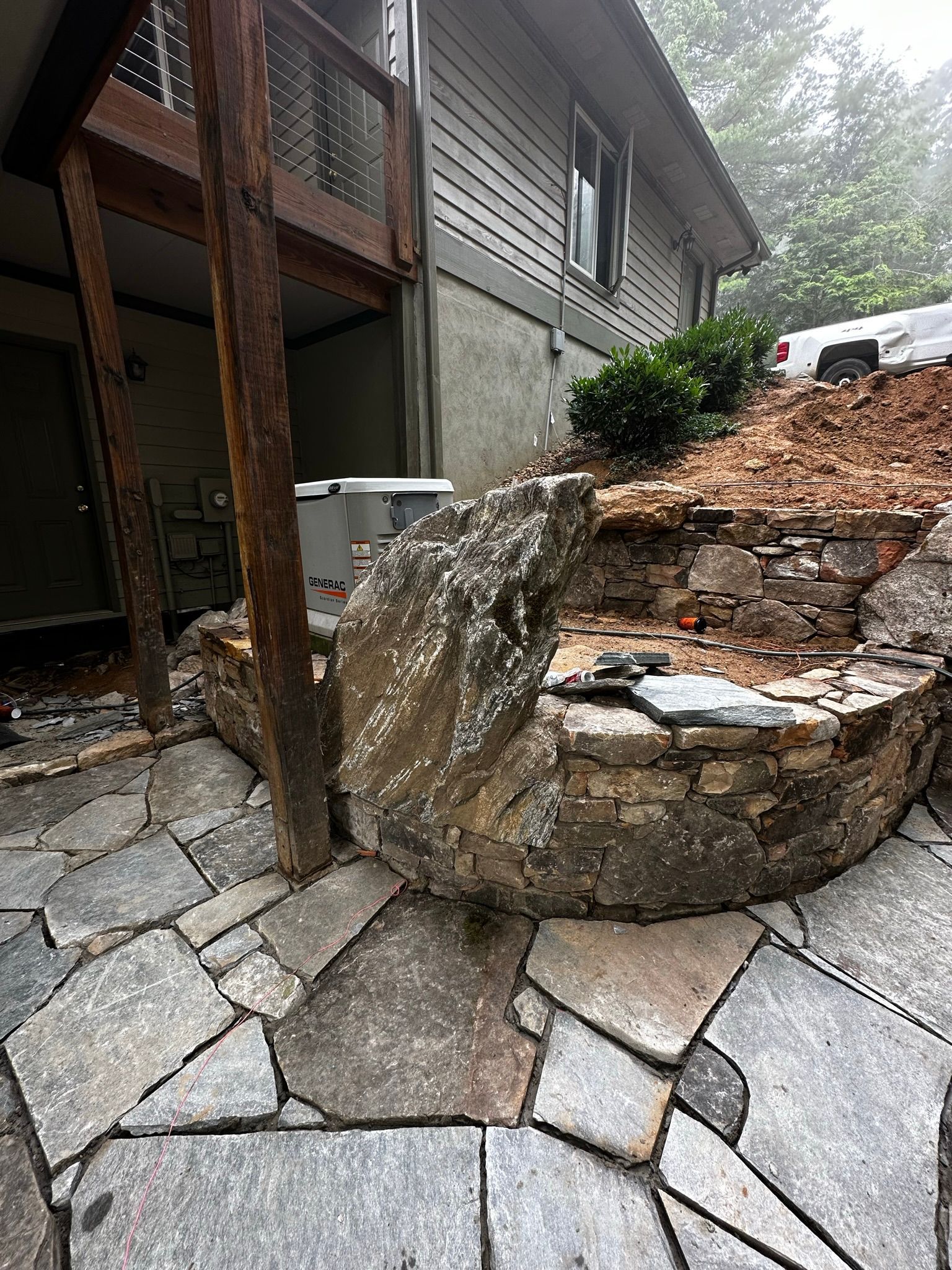 A large rock is sitting on top of a stone patio in front of a house.
