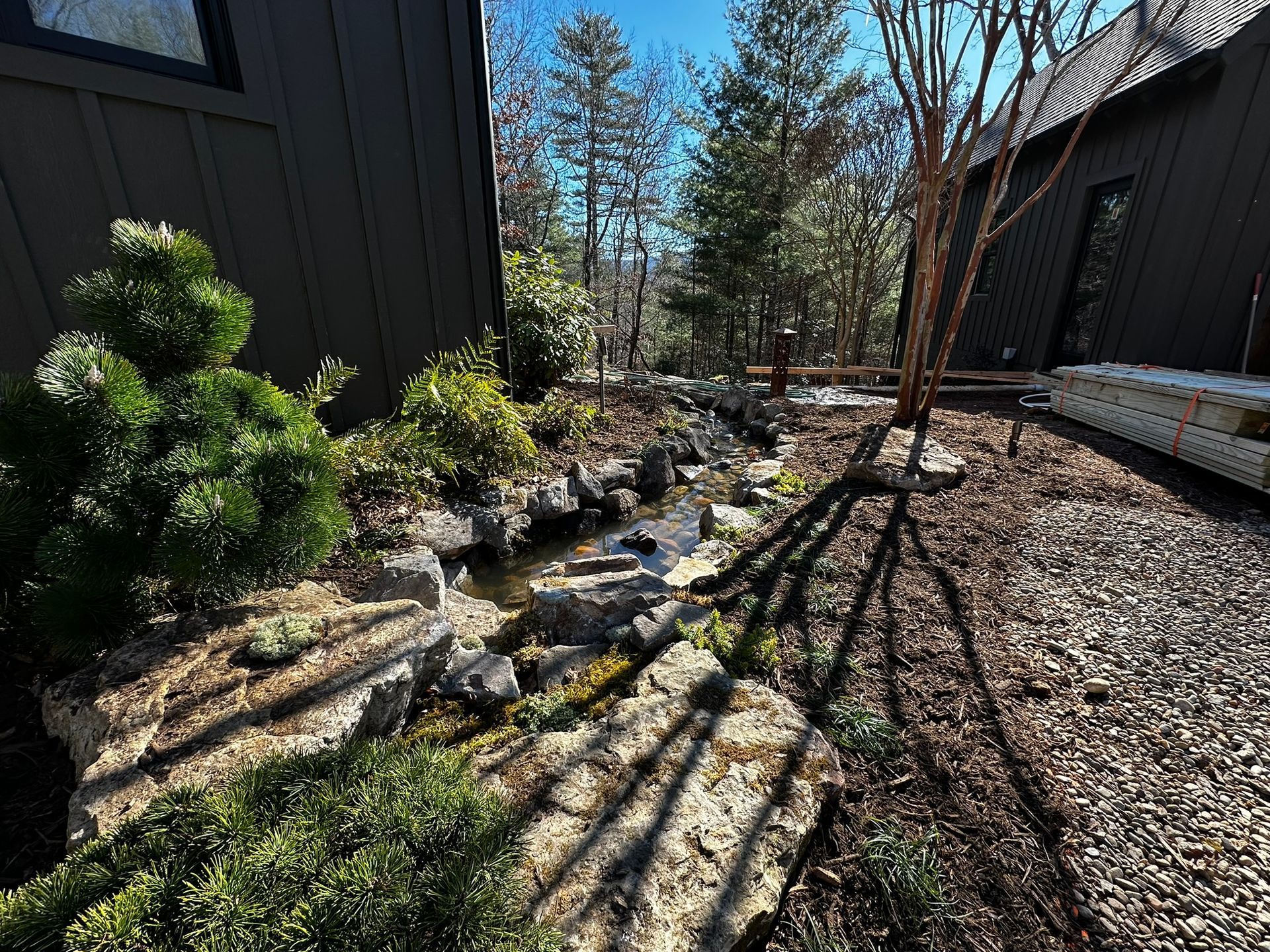 A stream running through a lush green garden next to a house.