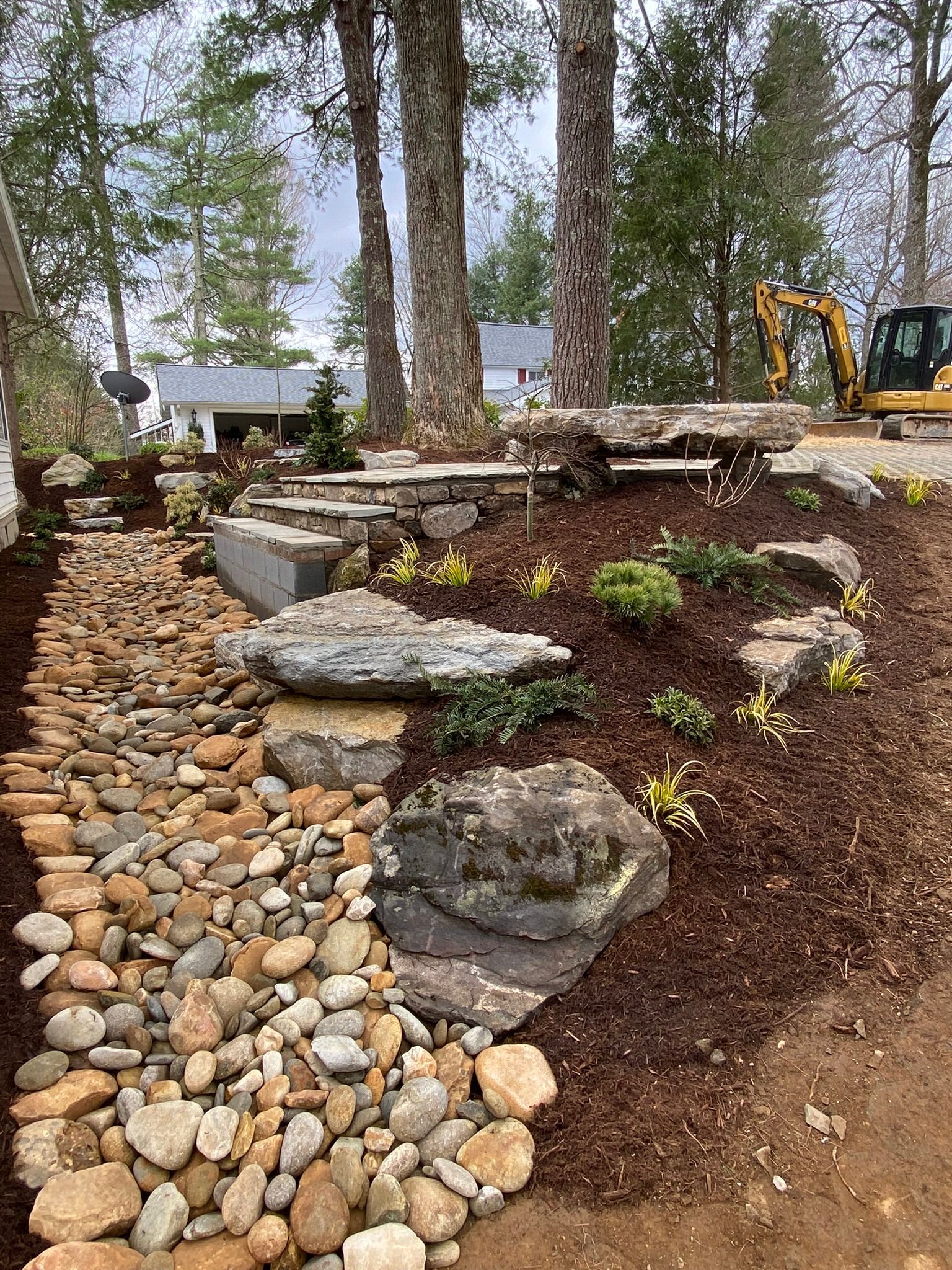 A large pile of rocks is sitting on top of a dirt hill next to a house.
