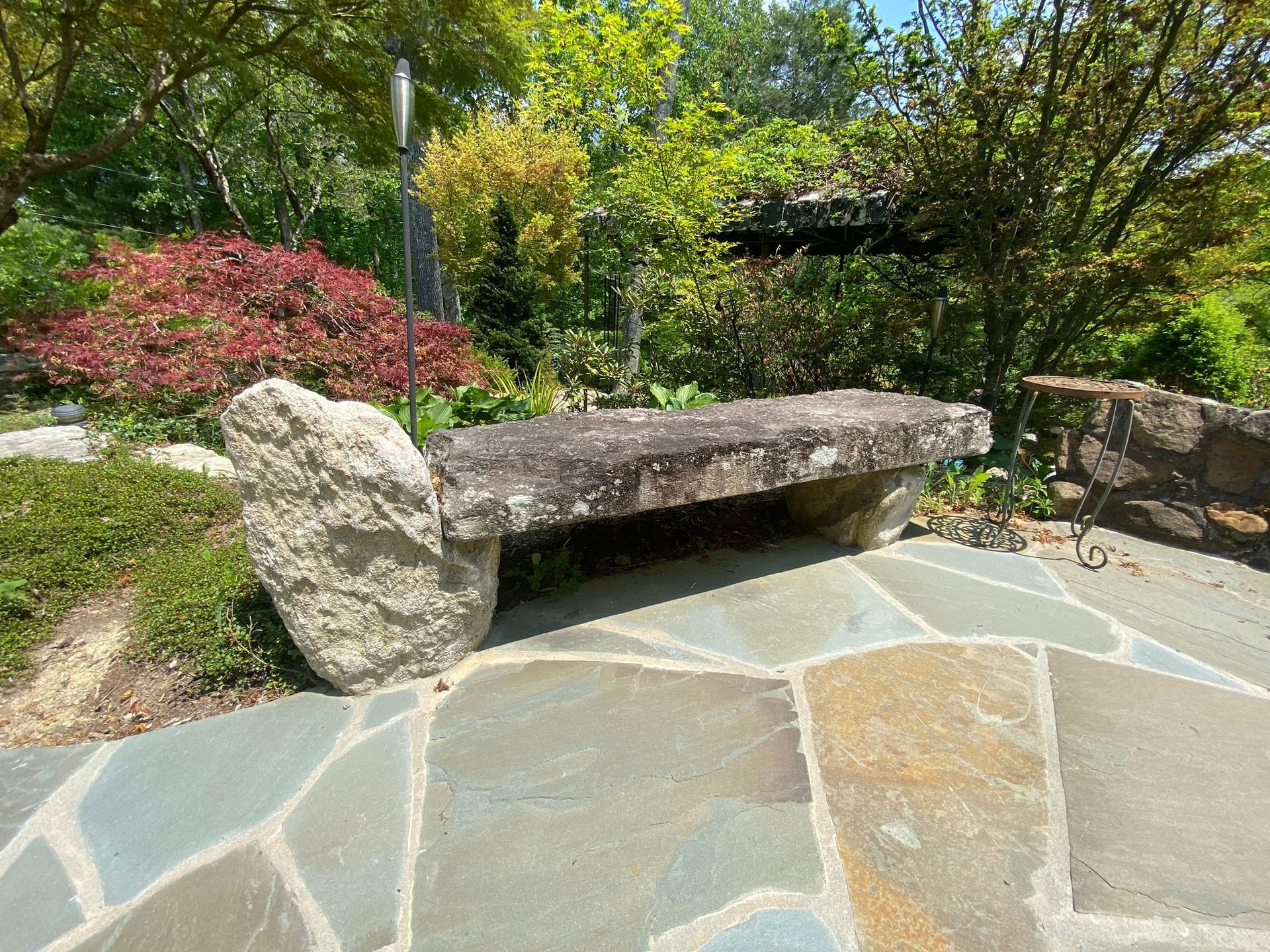 A stone bench is sitting on a stone walkway in a garden.