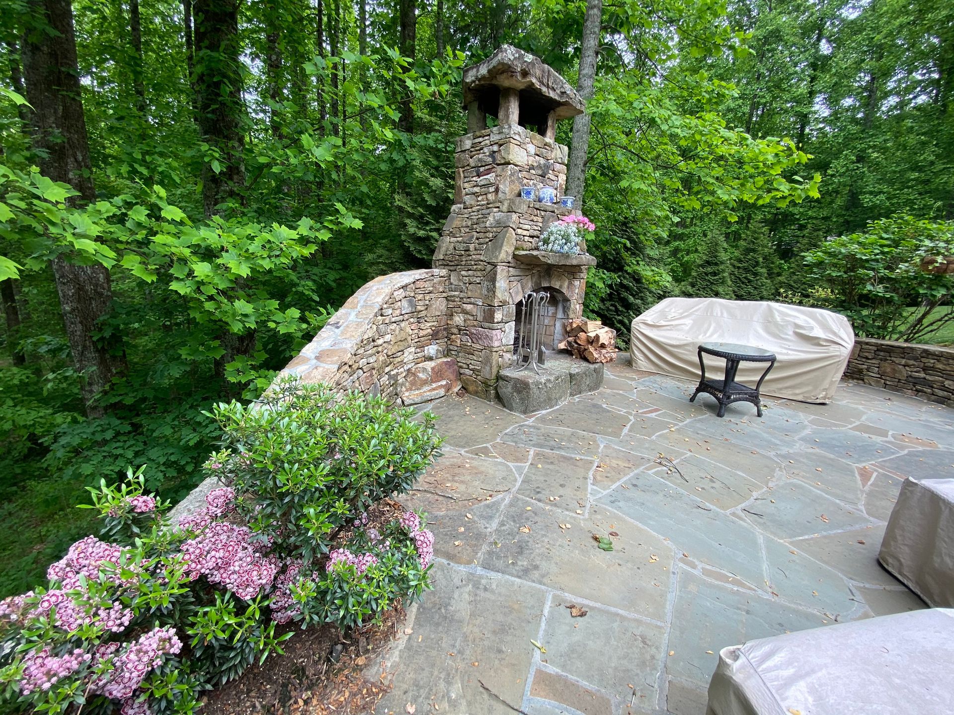 A stone fireplace is sitting on top of a stone patio surrounded by trees.