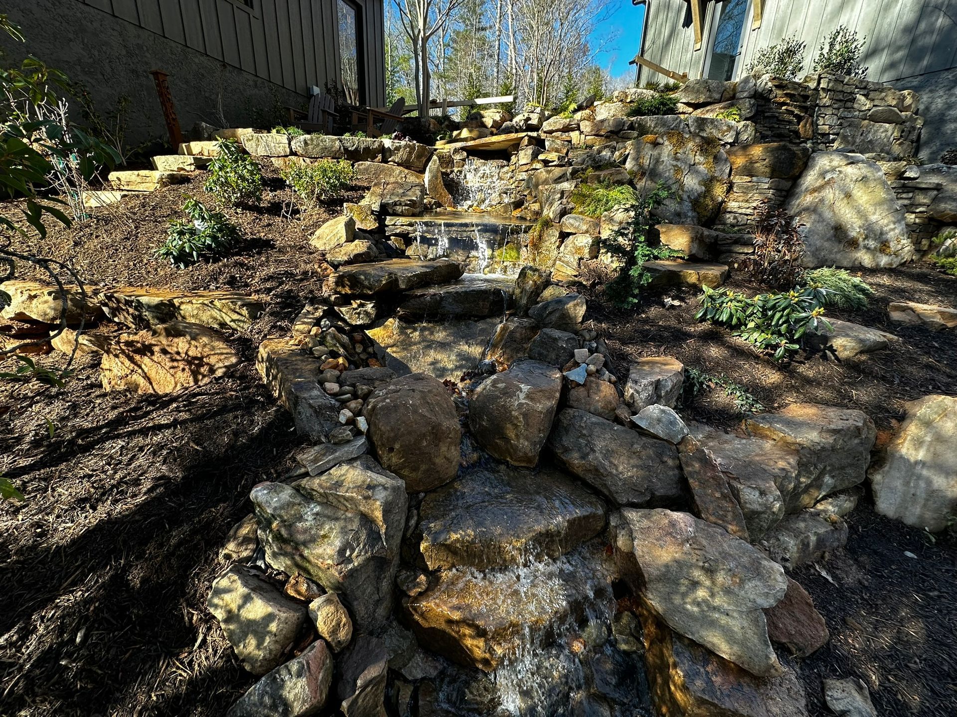 A waterfall is surrounded by rocks in a backyard.
