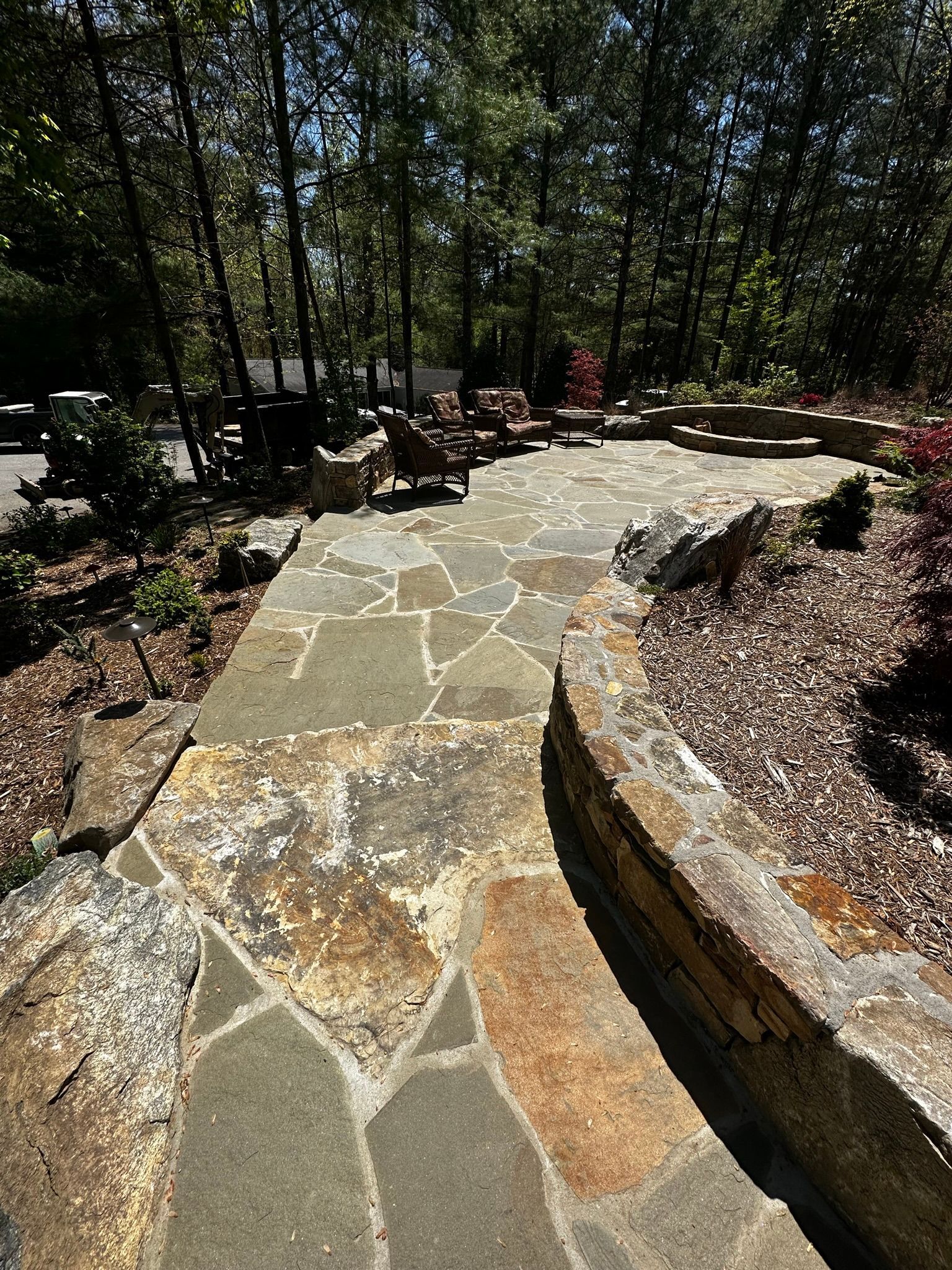 A stone walkway leading to a patio with chairs and trees in the background.