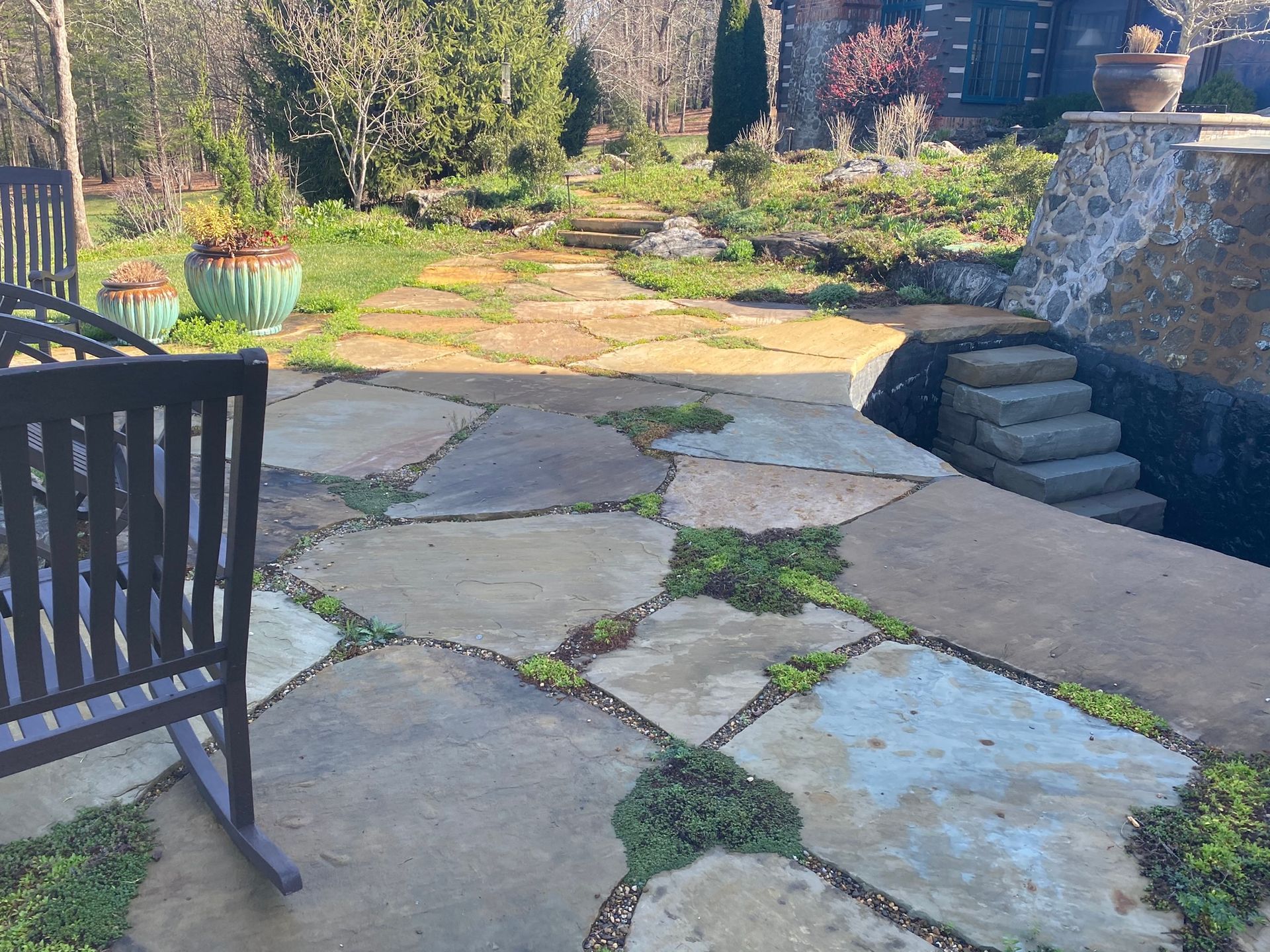 A rocking chair is sitting on a stone patio in a garden.