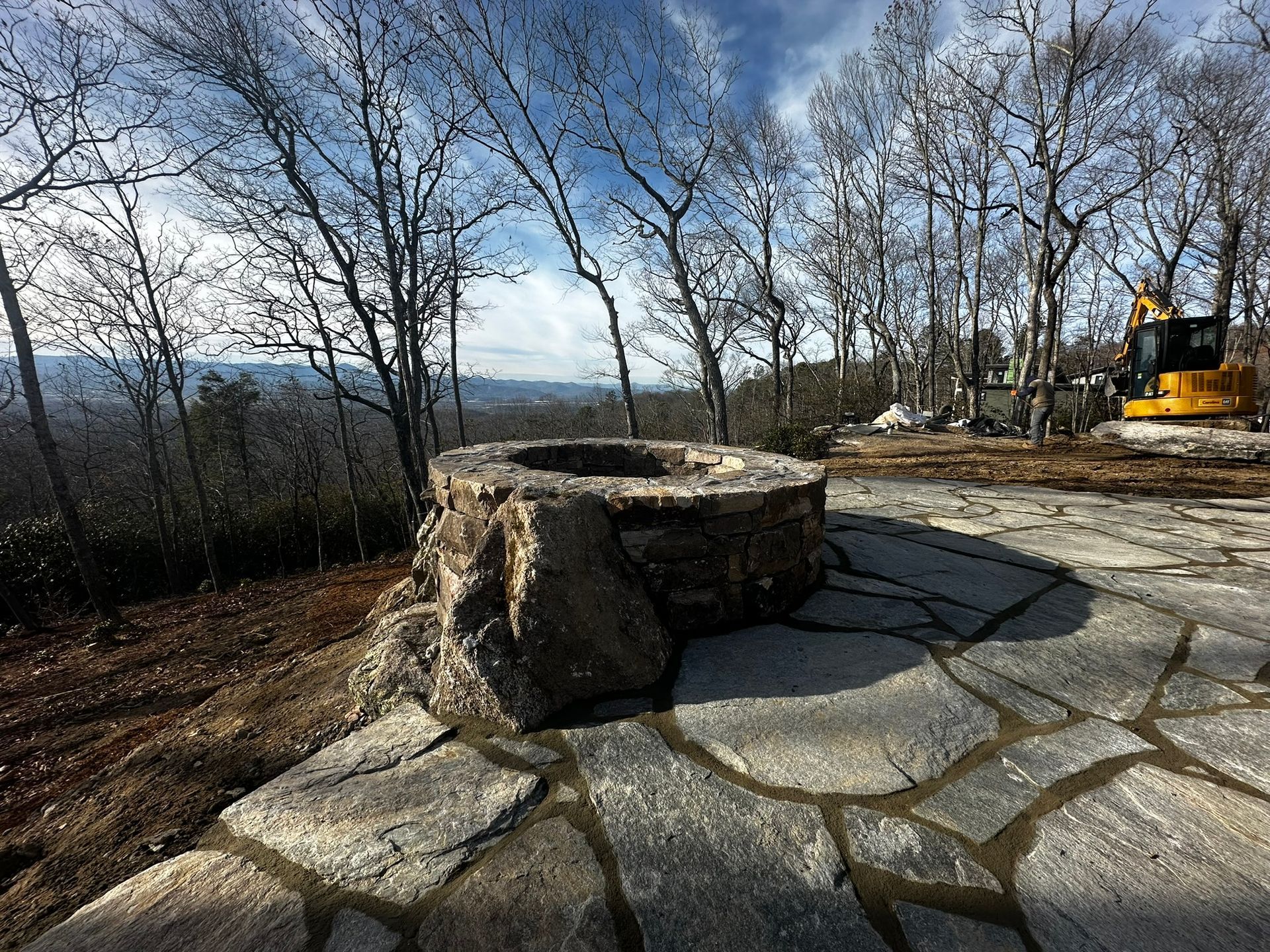 A fire pit is sitting on top of a stone patio with trees in the background.