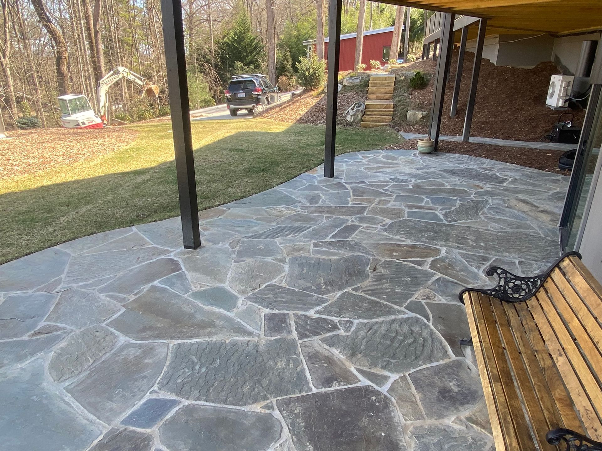 A stone patio with a bench and a car parked in the background.