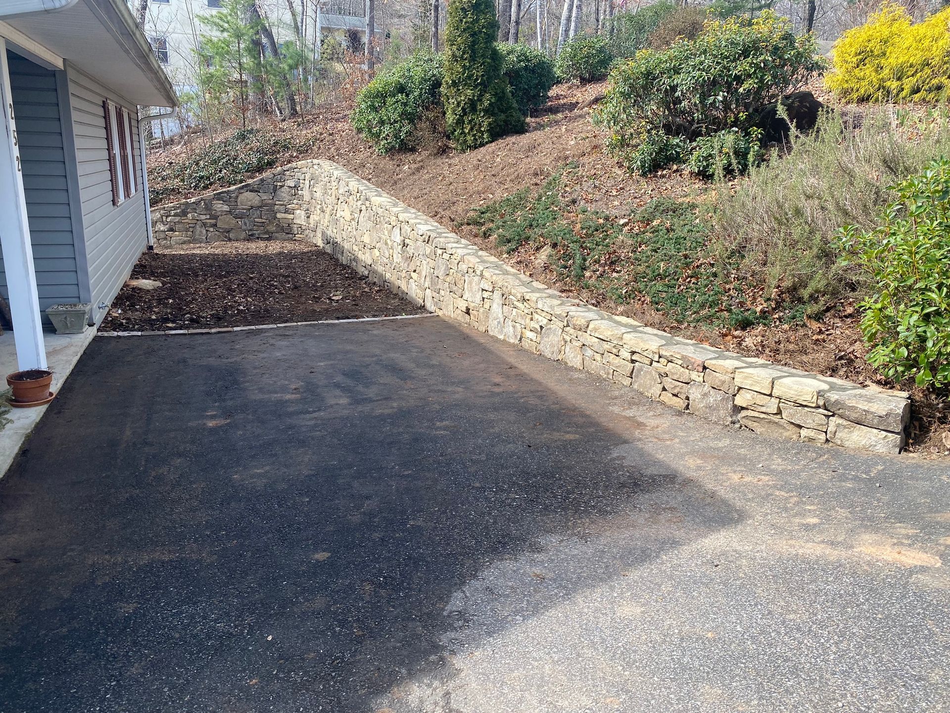A driveway leads to a house with a stone wall.