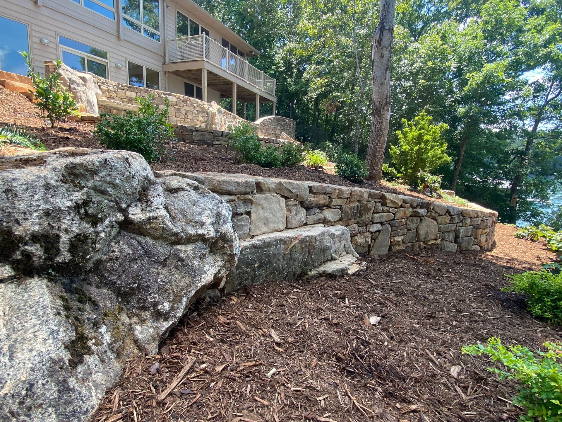 A large stone wall surrounds a house on a hill overlooking a lake.