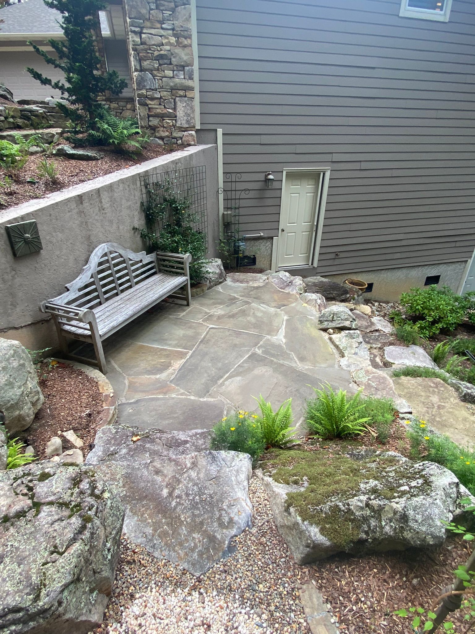 A stone patio with a bench and rocks in front of a house.
