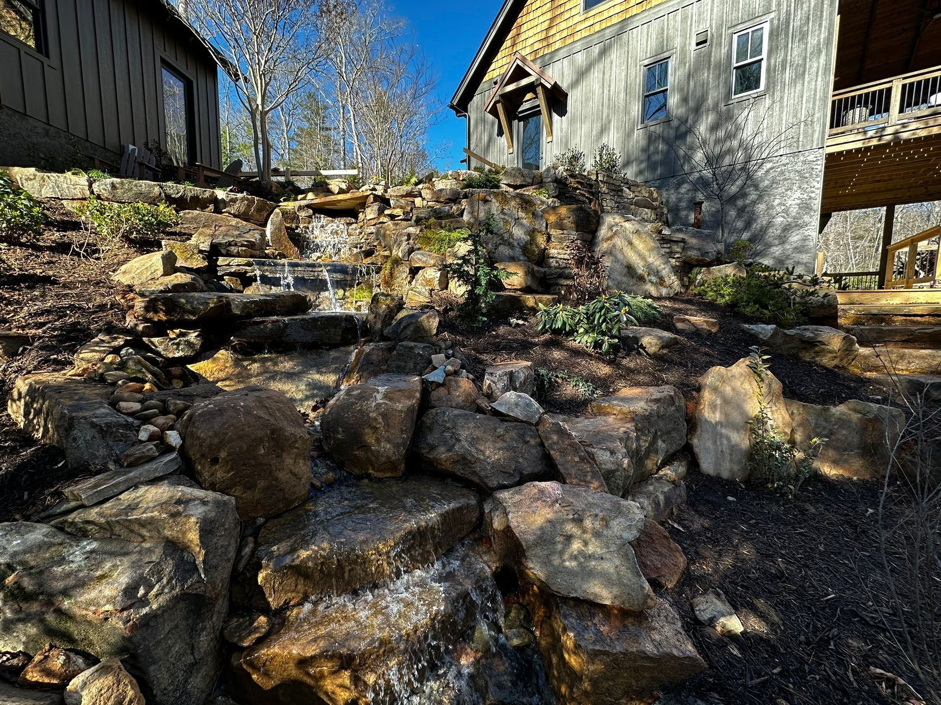 A waterfall is surrounded by rocks in front of a house.