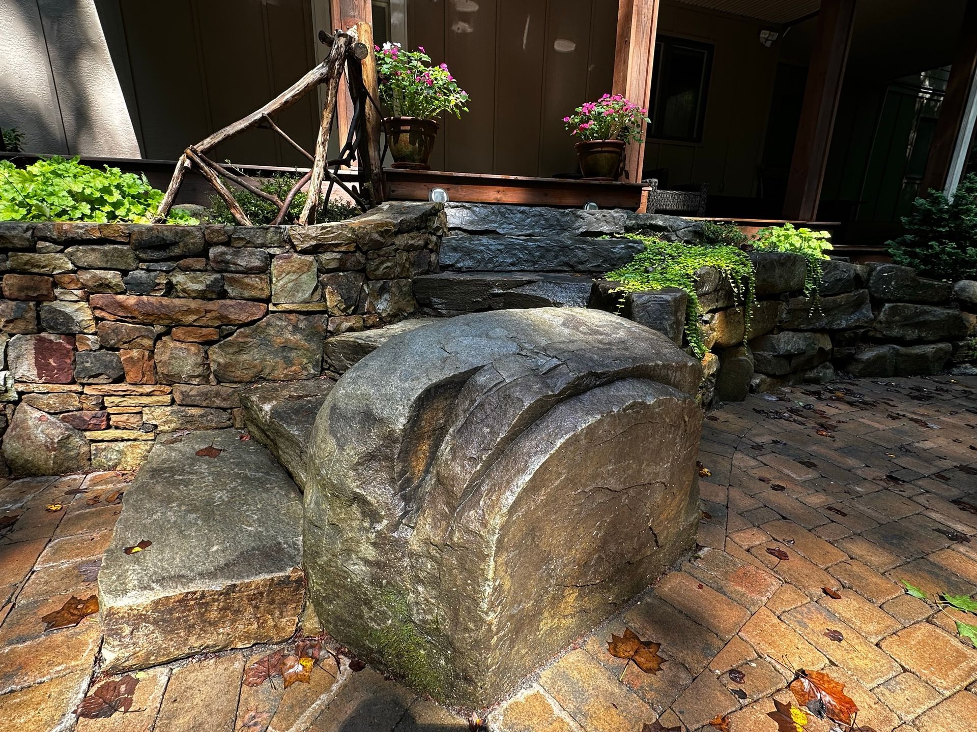 A stone bench is sitting on a brick patio in front of a stone wall.