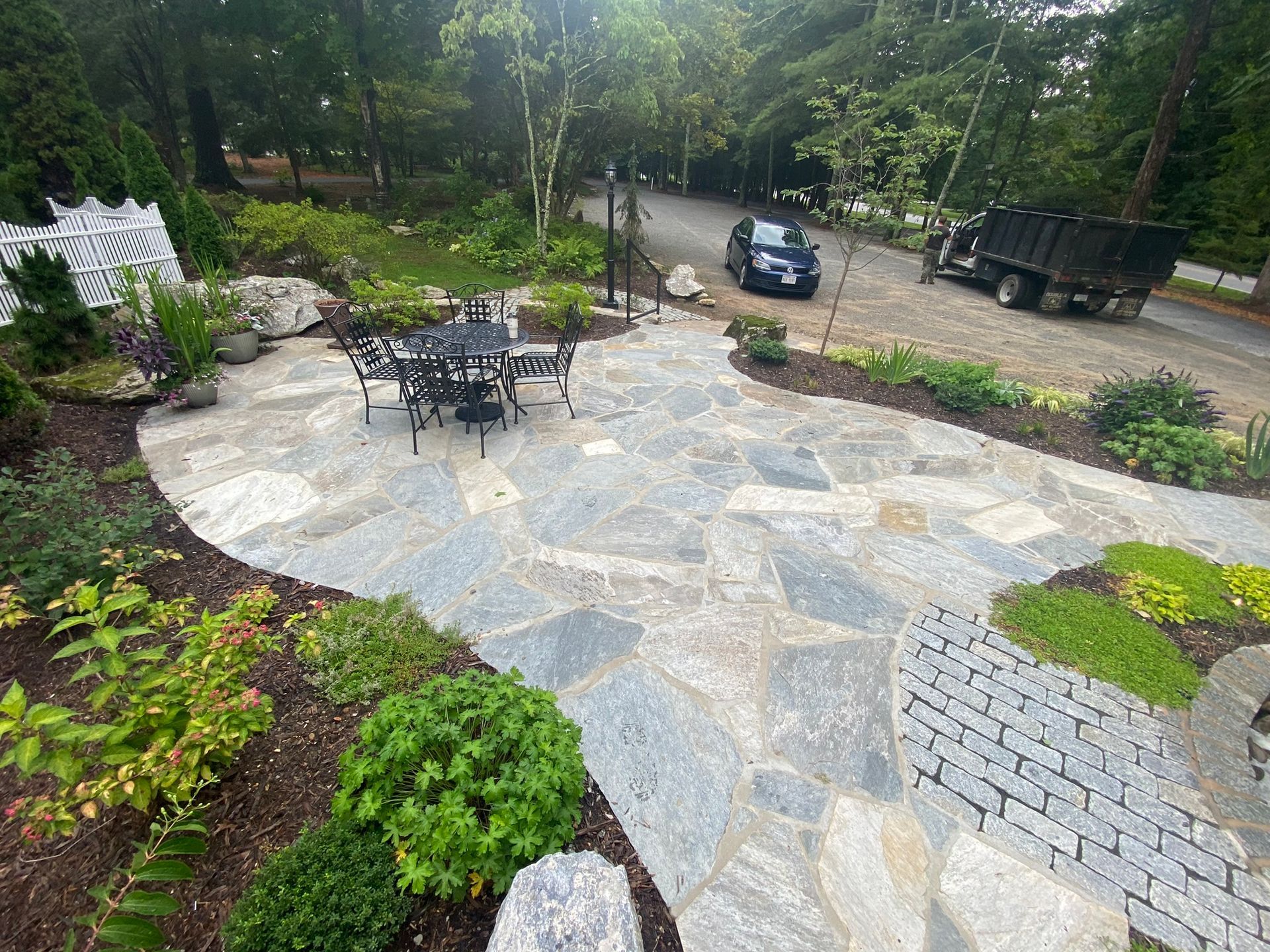 A car is driving down a road next to a patio with a table and chairs.