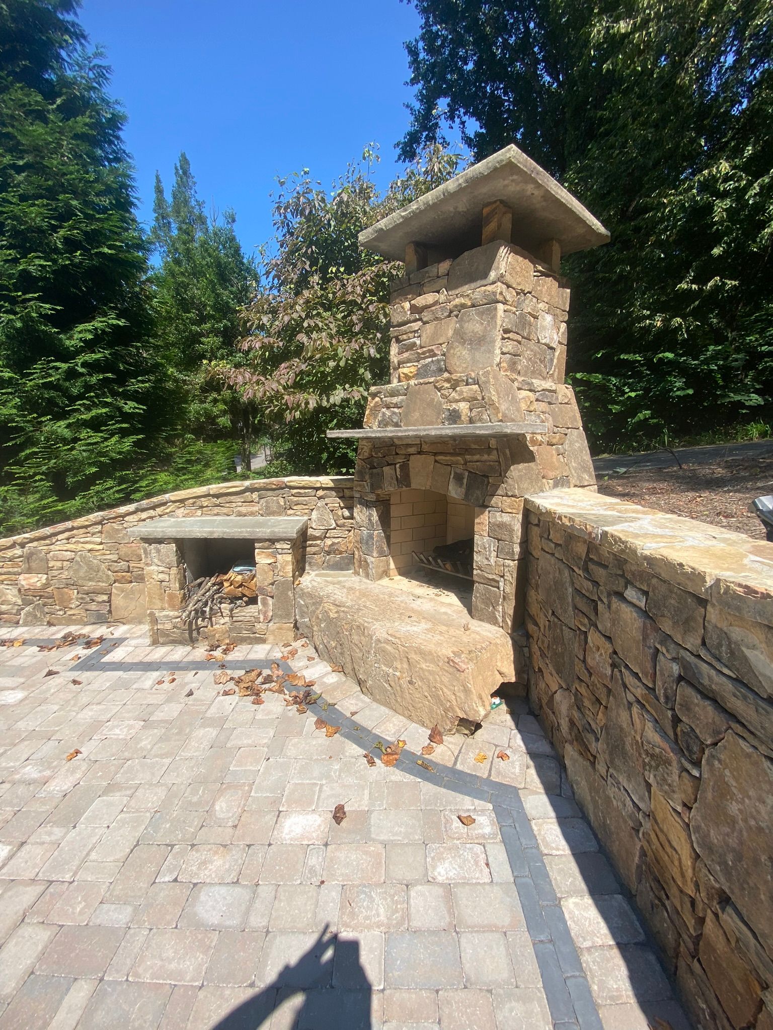A stone fireplace is sitting on top of a brick patio next to a stone wall.