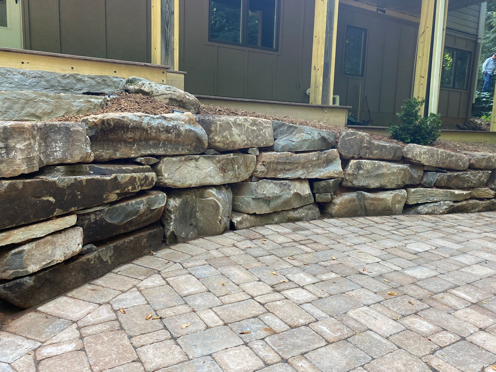 A stone wall surrounds a brick patio in front of a house.