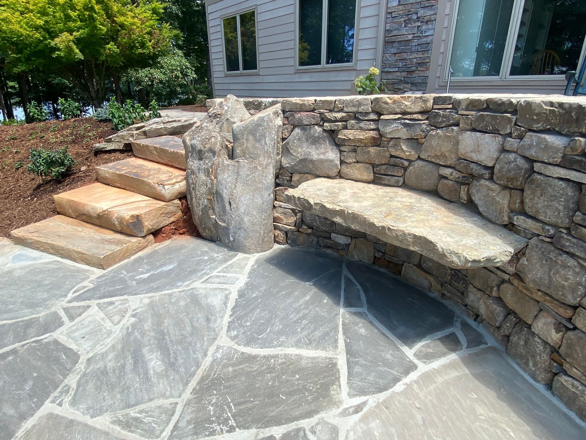 A stone wall with a bench and stairs in front of a house.
