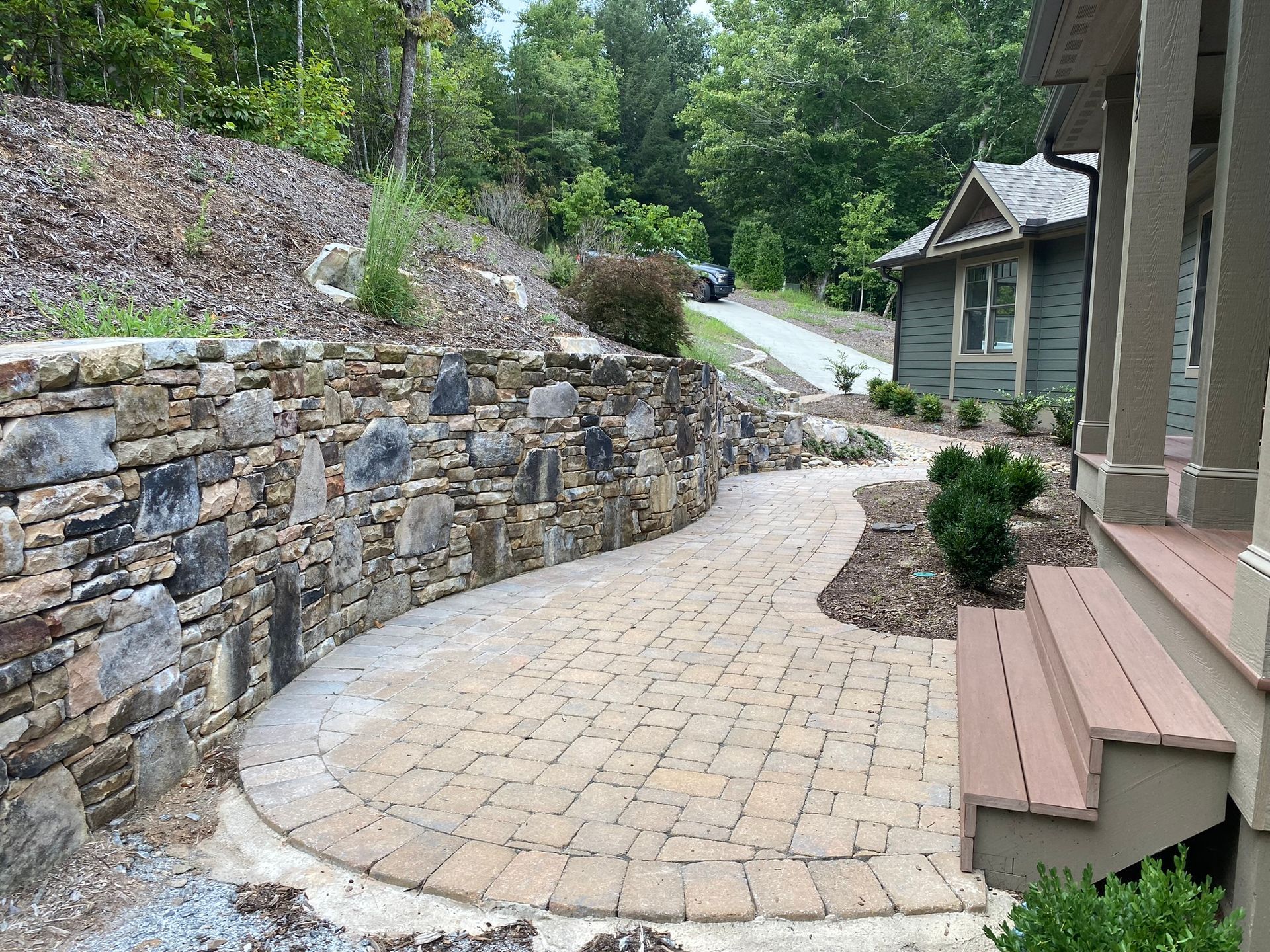 A stone wall surrounds a brick walkway leading to a house.