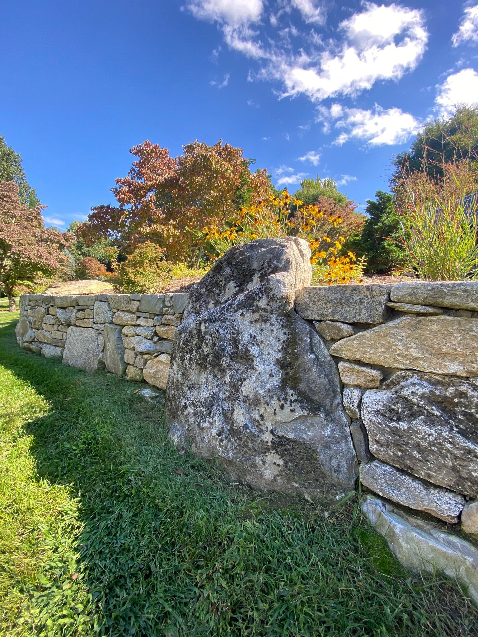 A stone wall surrounded by grass and trees on a sunny day.