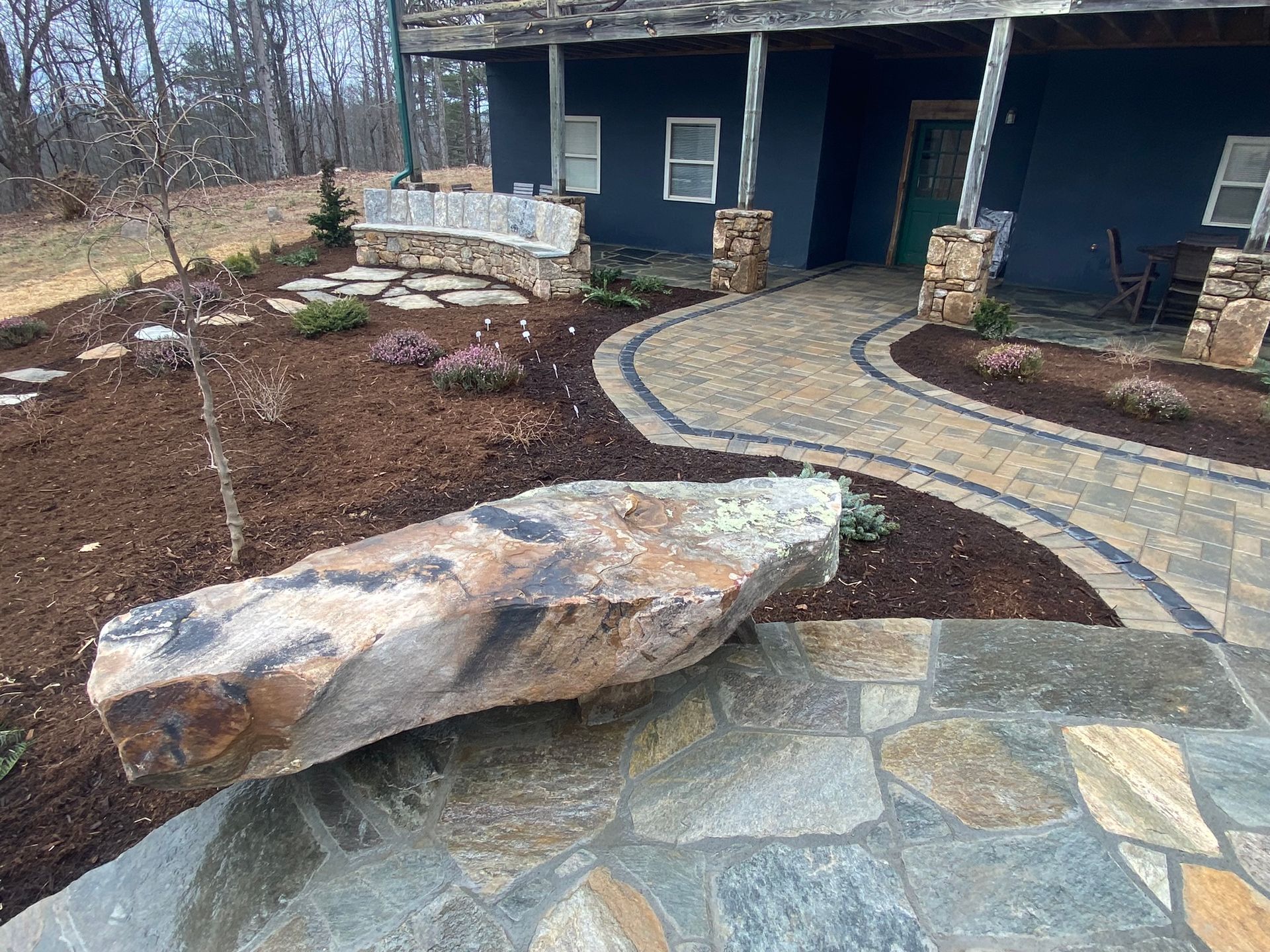 A large rock is sitting in front of a blue house.