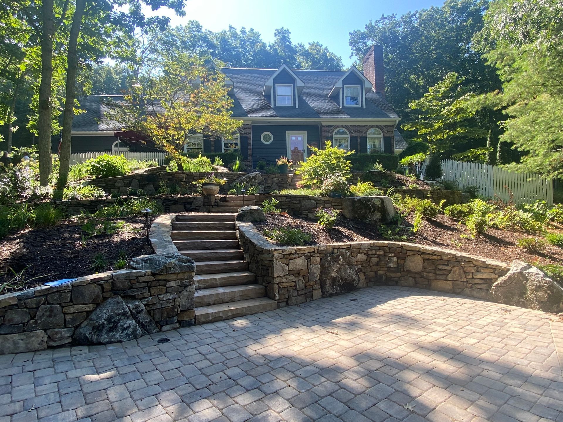 A large house with stairs leading up to it is surrounded by trees and bushes.
