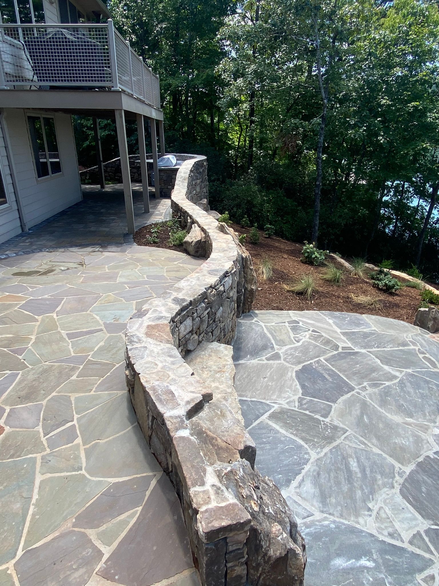 A patio with a stone wall and a bench in front of a house.