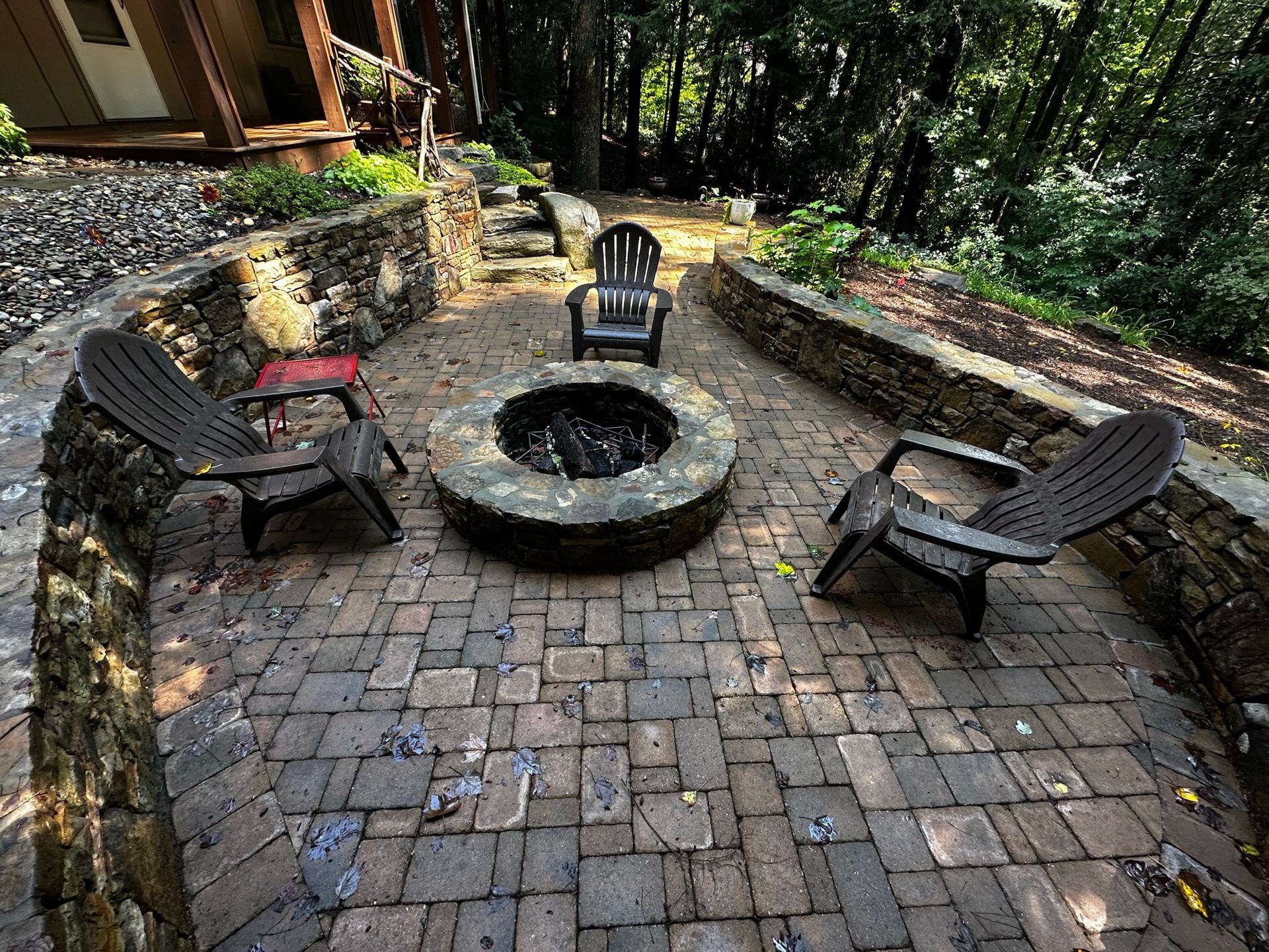 A fire pit is surrounded by chairs on a brick patio.
