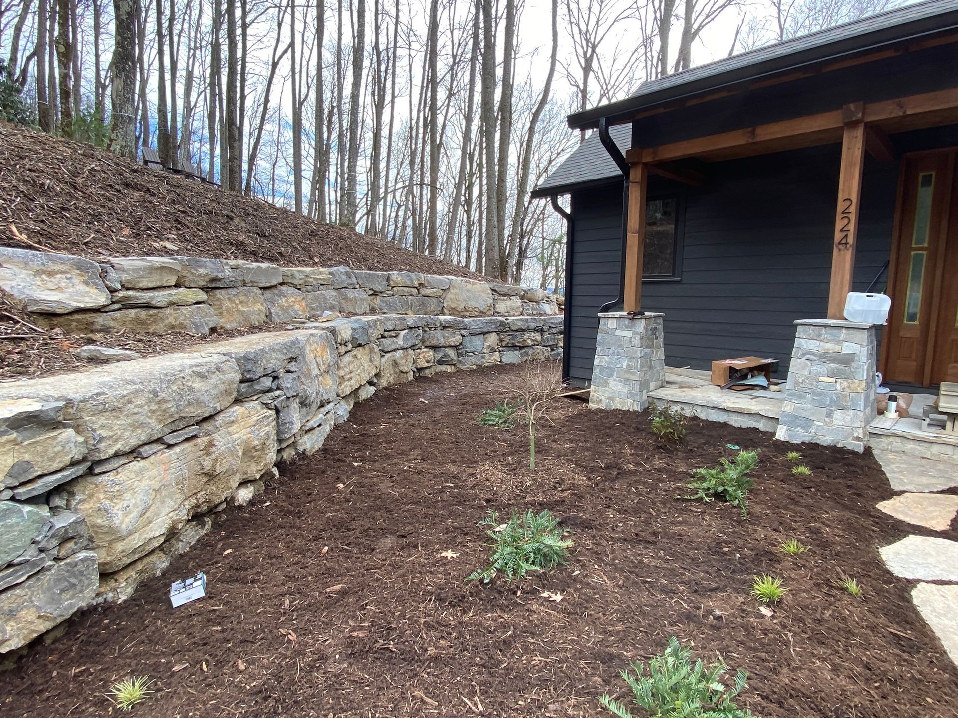 A stone wall is surrounding a house in the woods.