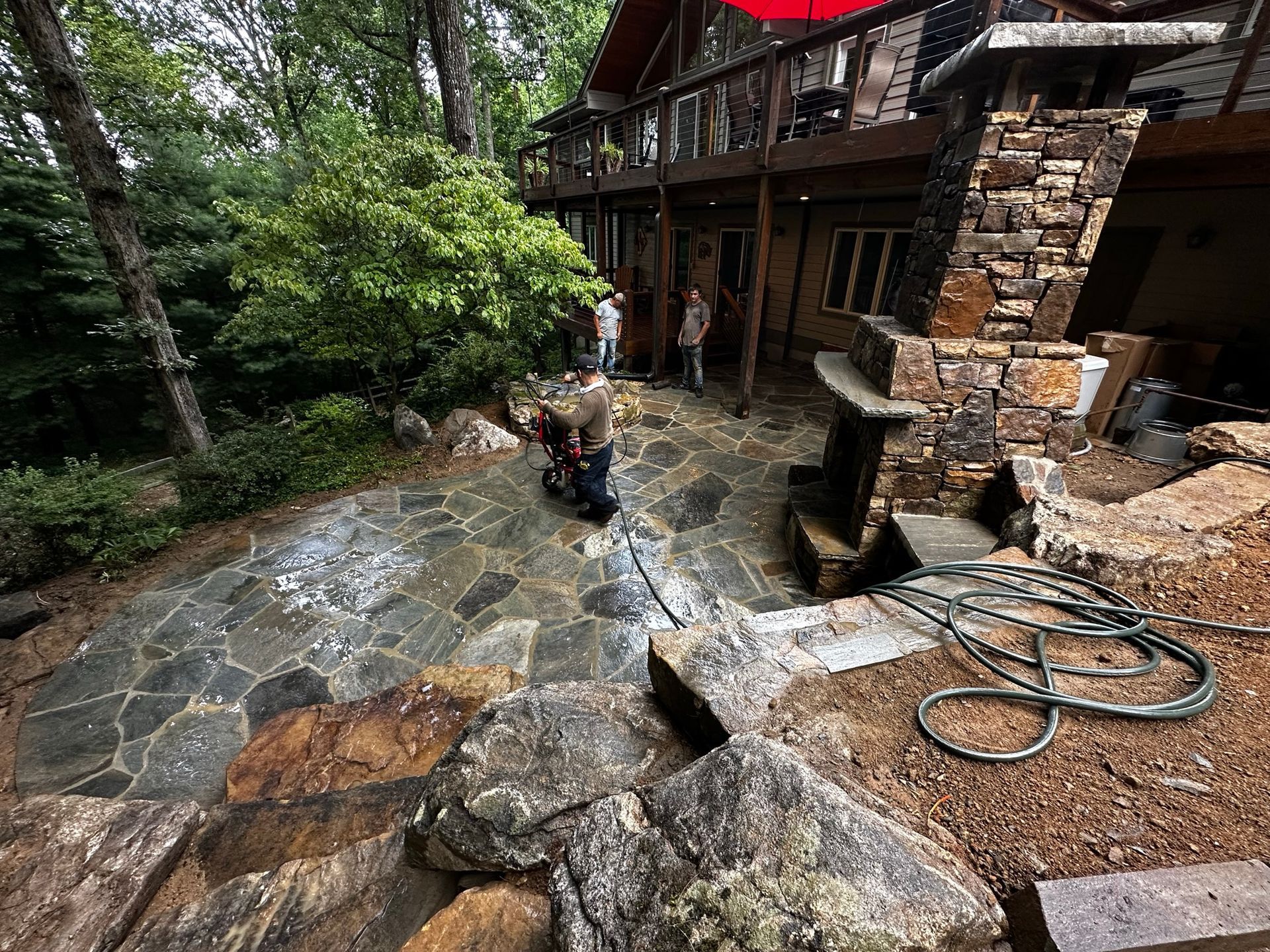A group of people are working on a stone patio in front of a house.