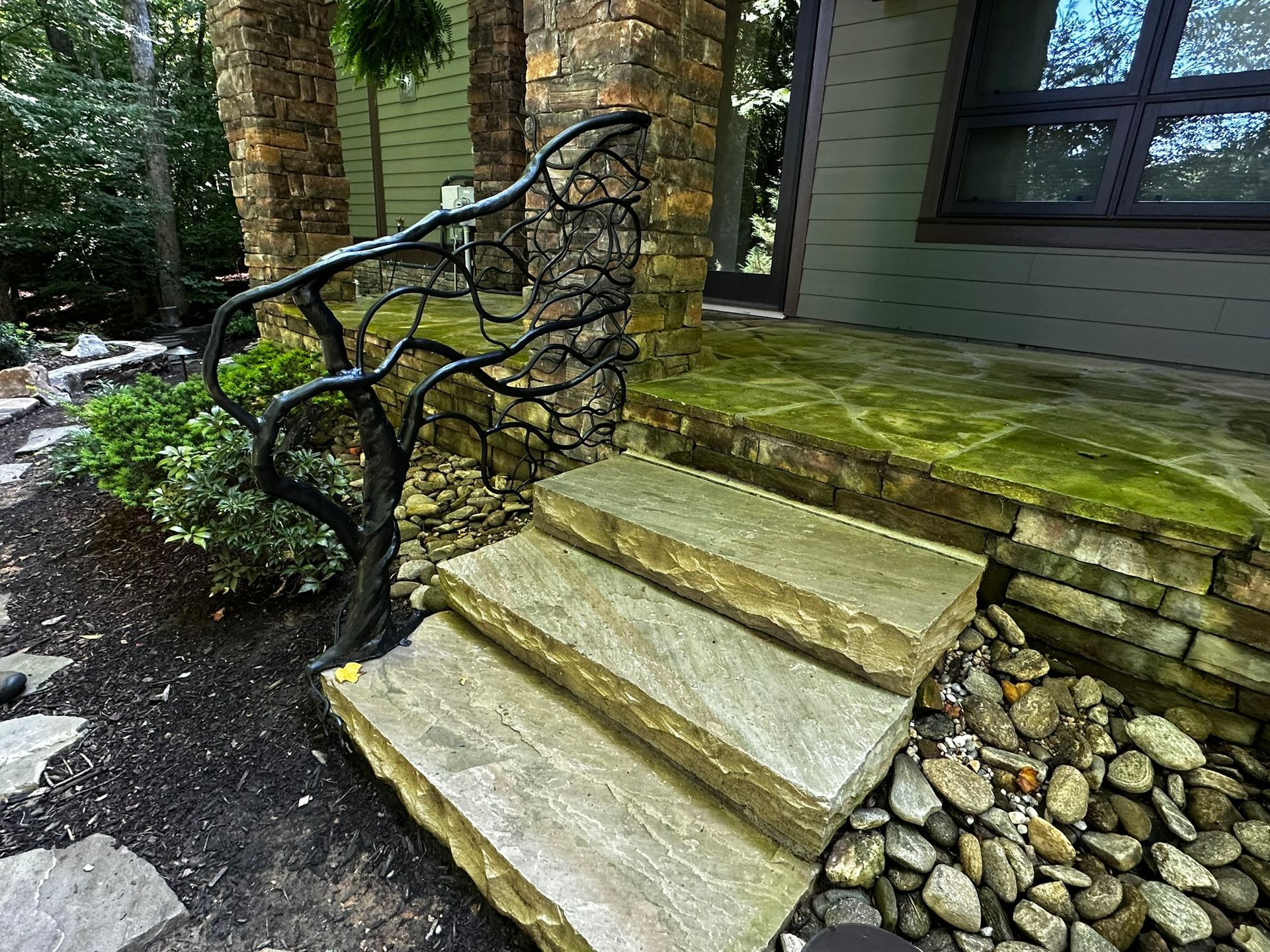 A set of stairs leading up to a stone porch with a wrought iron railing.