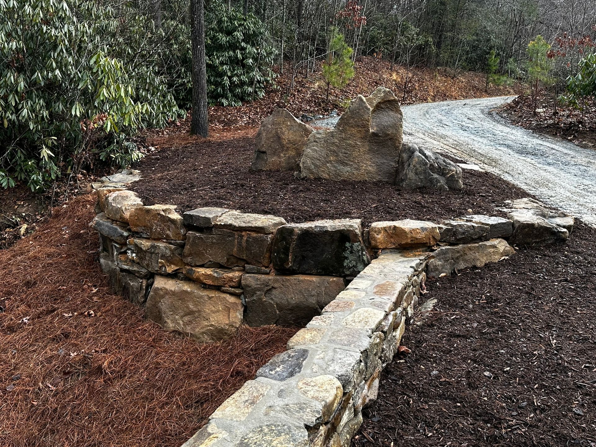 A stone wall surrounds a gravel path in a garden.
