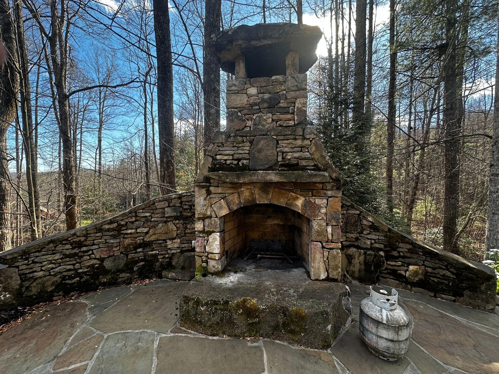 There is a stone fireplace in the middle of the woods.