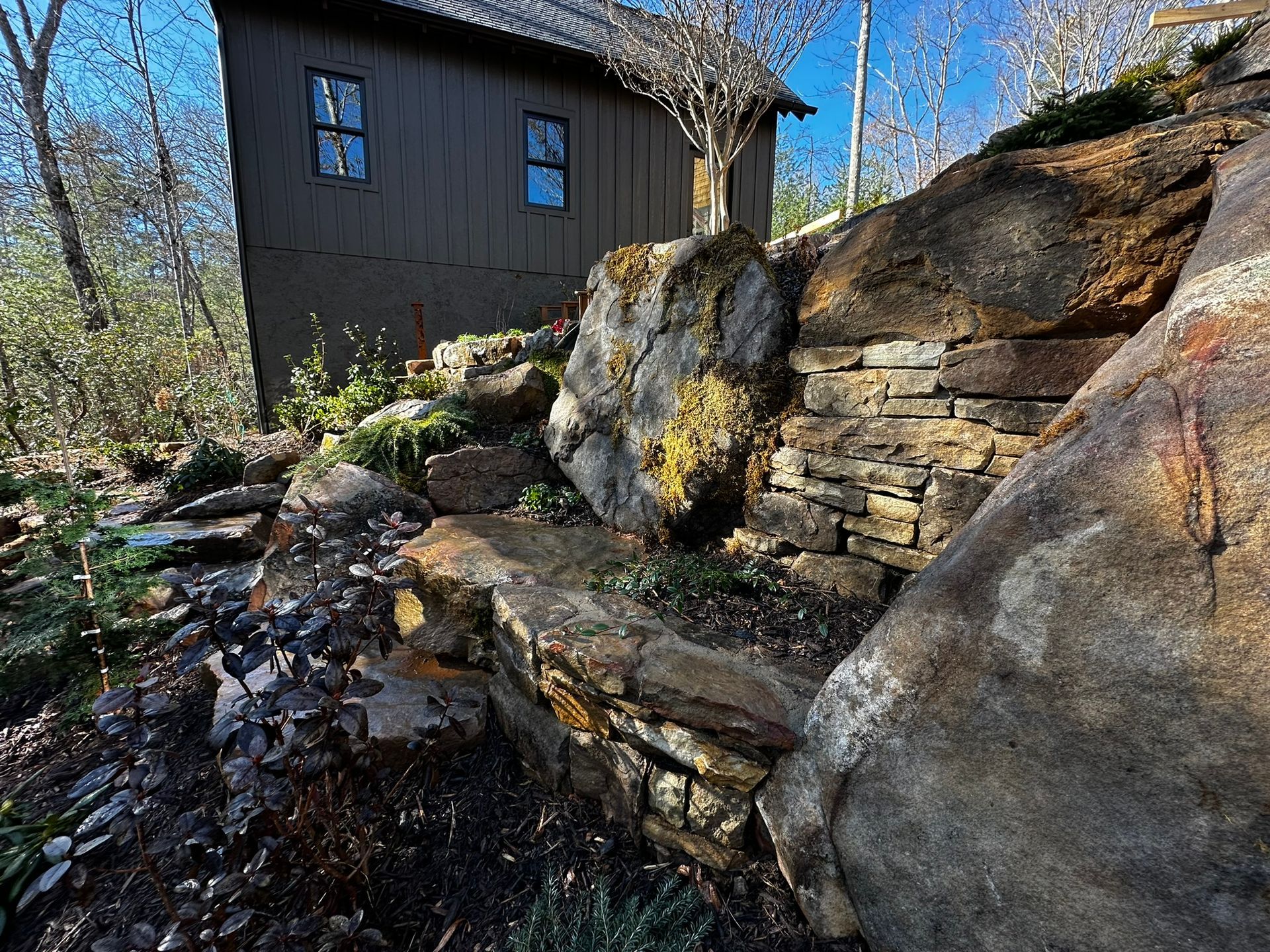 A house is sitting on top of a rocky hill next to a stone wall.
