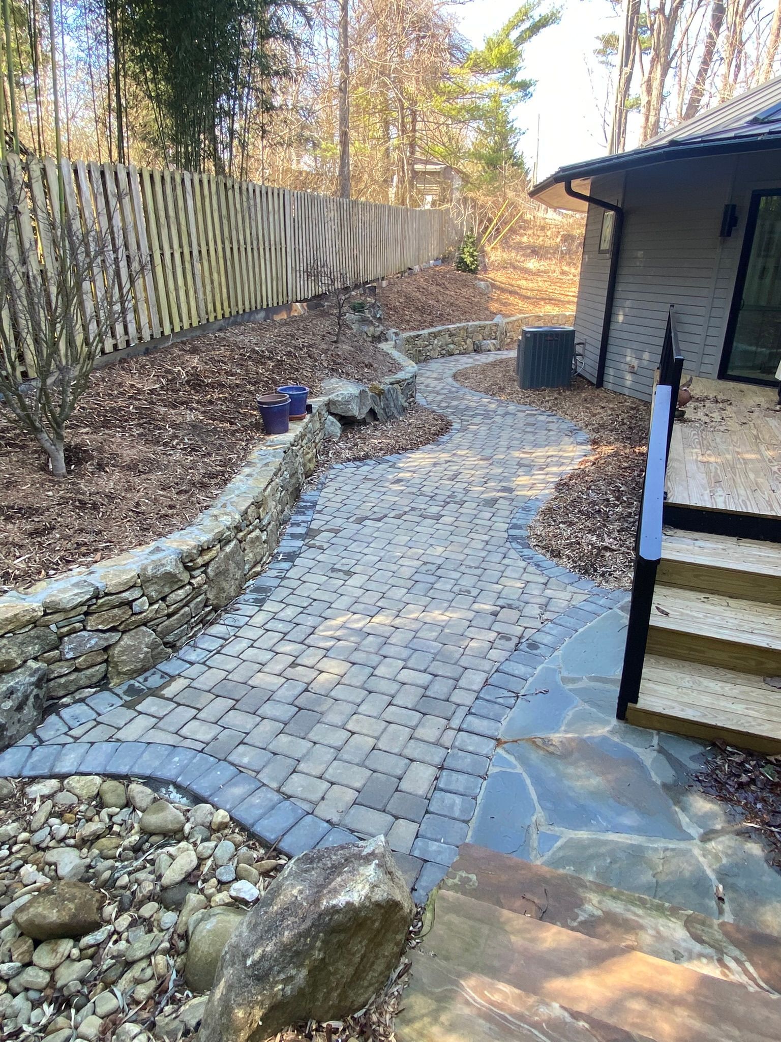 A brick walkway leading to a house with stairs and a stone wall.