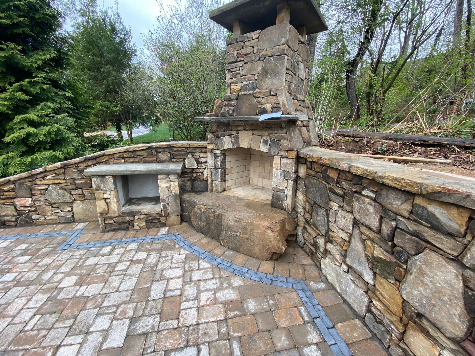A stone fireplace is sitting on top of a brick patio next to a stone wall.