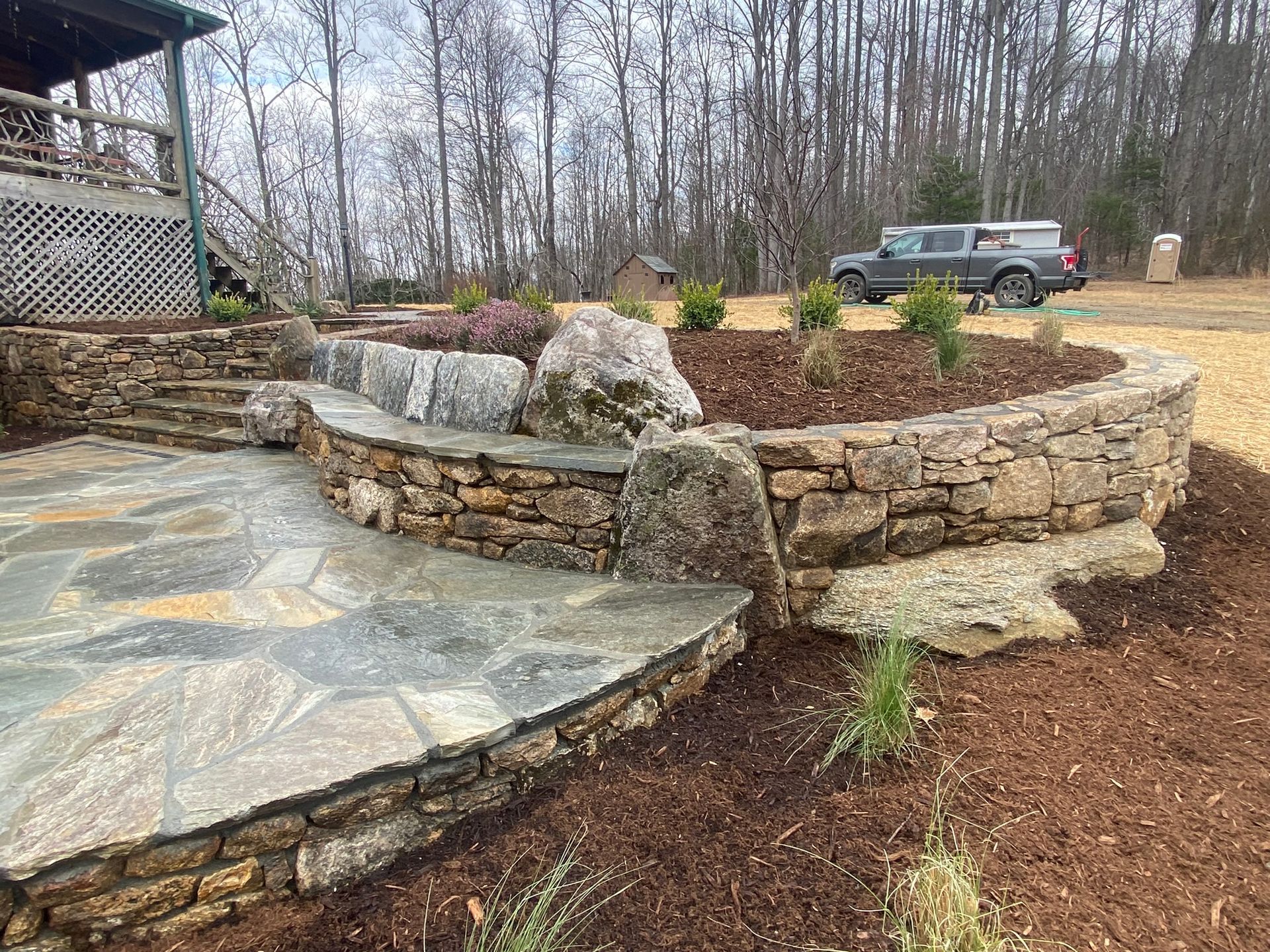 A truck is parked in front of a stone wall in a yard.
