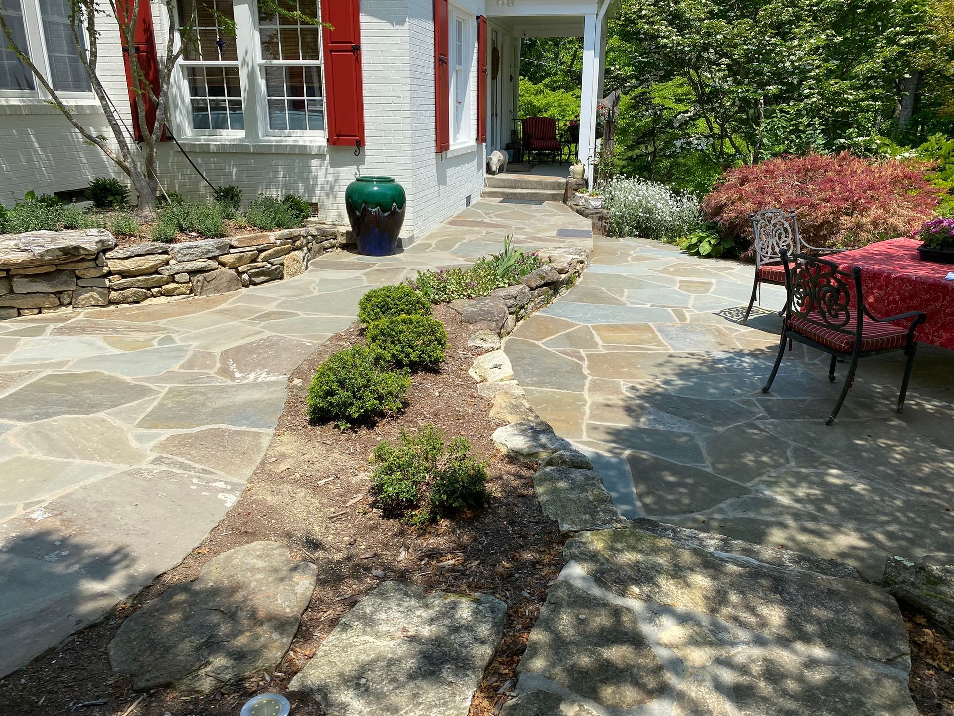 A stone walkway leading to a patio with a table and chairs in front of a white house.