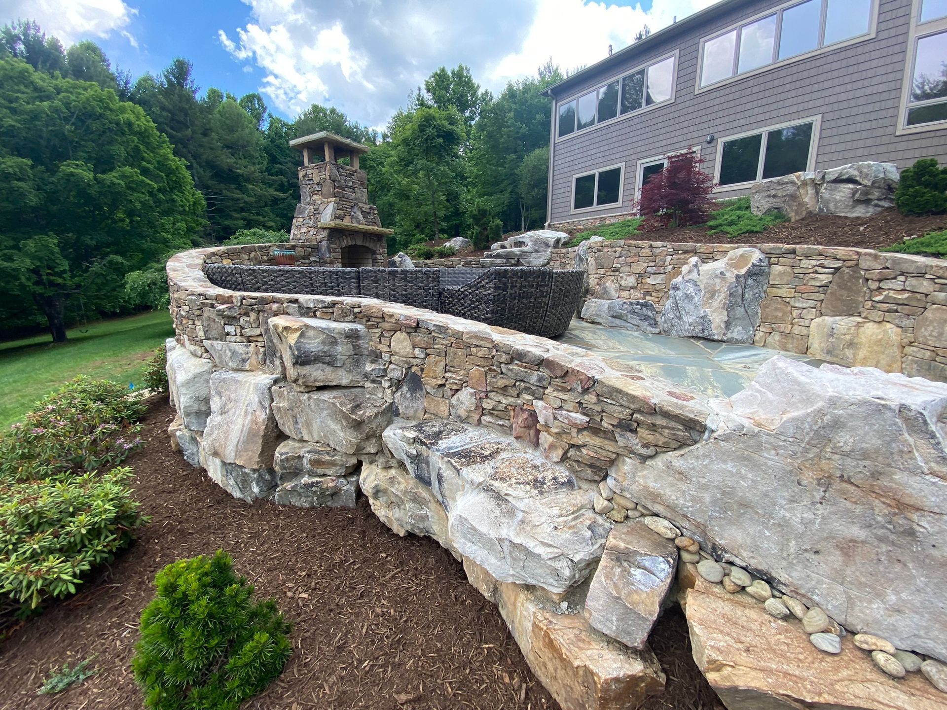 A large stone wall with a waterfall in front of a house.