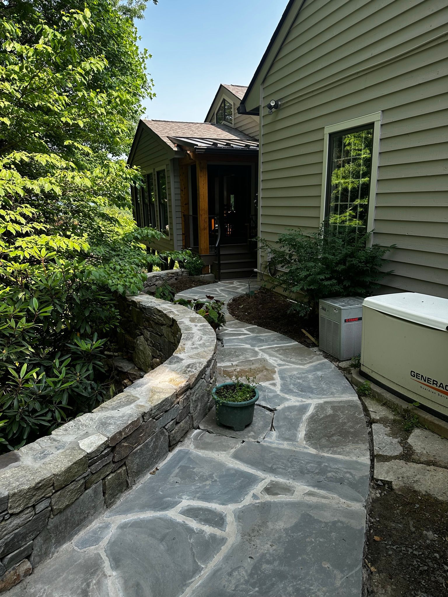 A stone walkway leading to a house with a generator in the backyard.