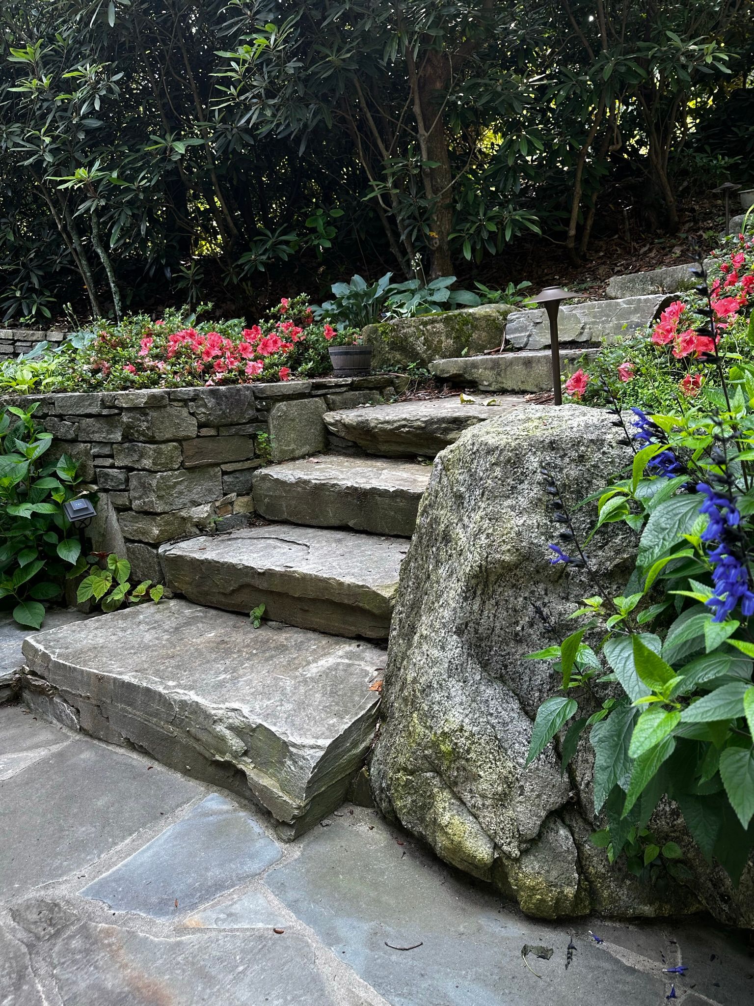 A stone staircase leading up to a rock wall surrounded by flowers.