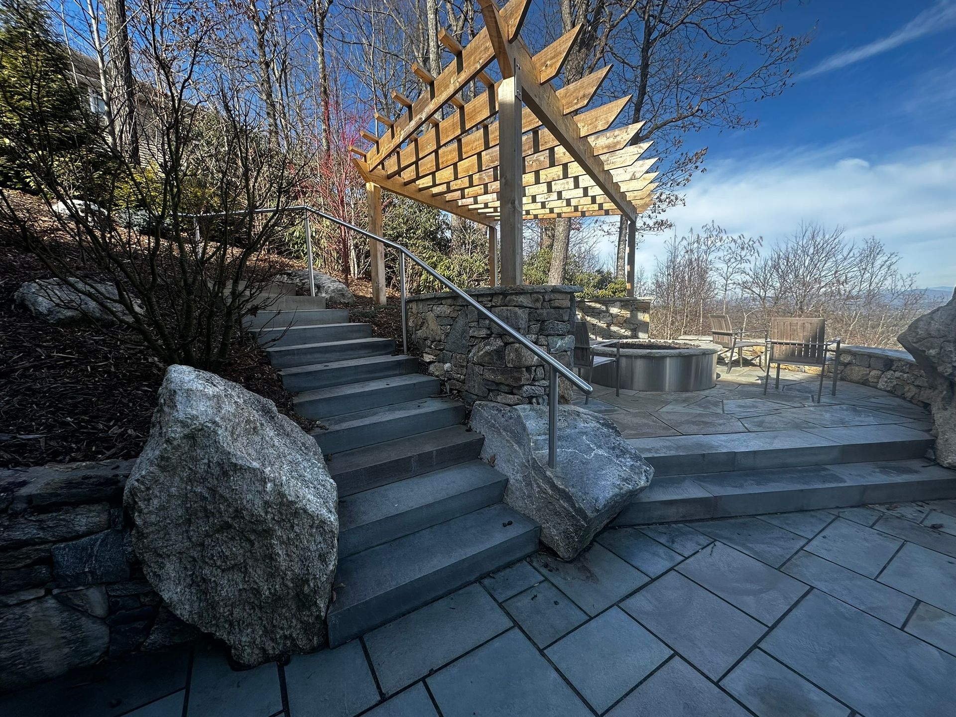 A stone patio with stairs leading up to a wooden pergola.