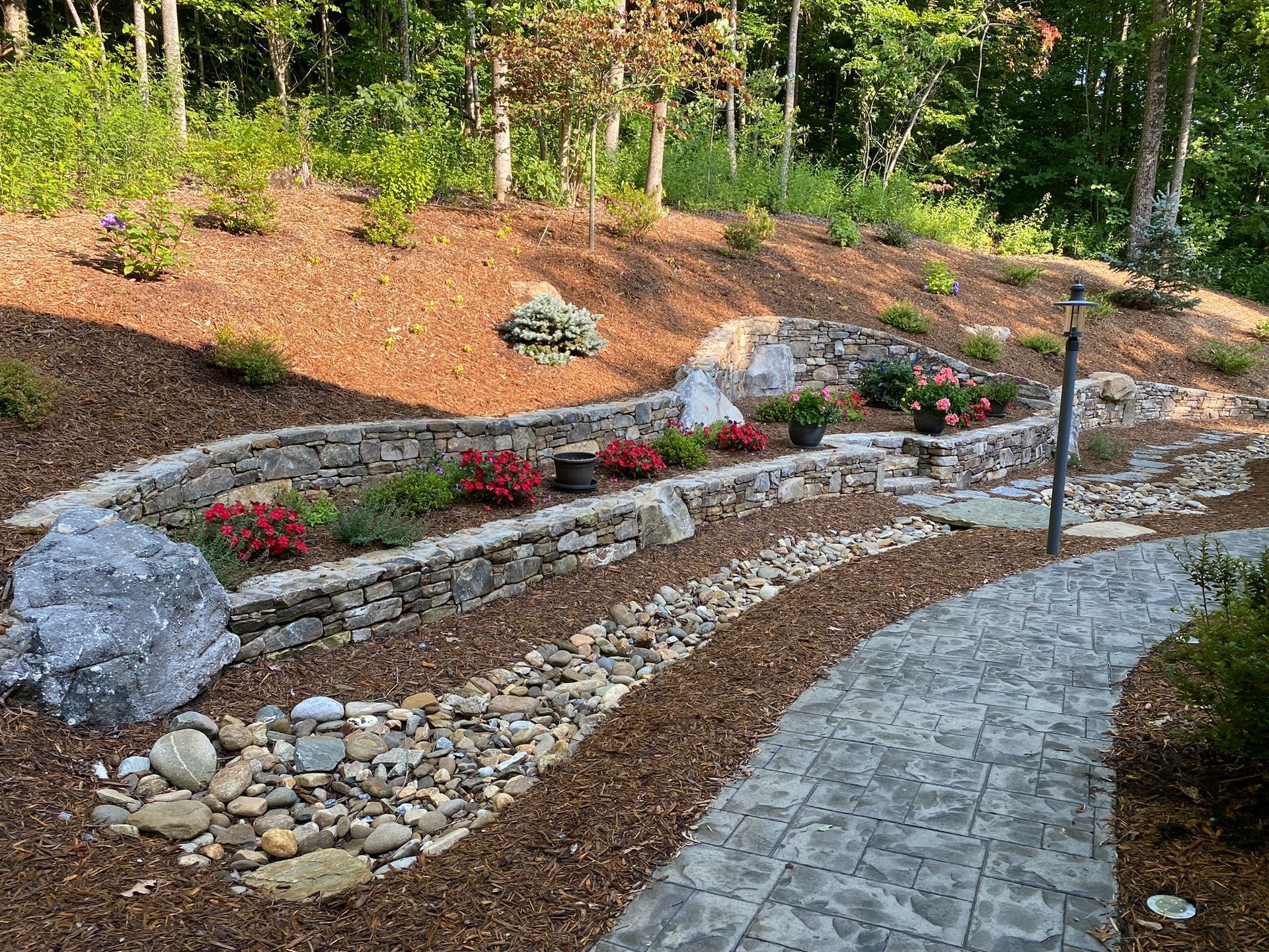 A stone walkway leading to a stone wall surrounded by rocks and flowers.