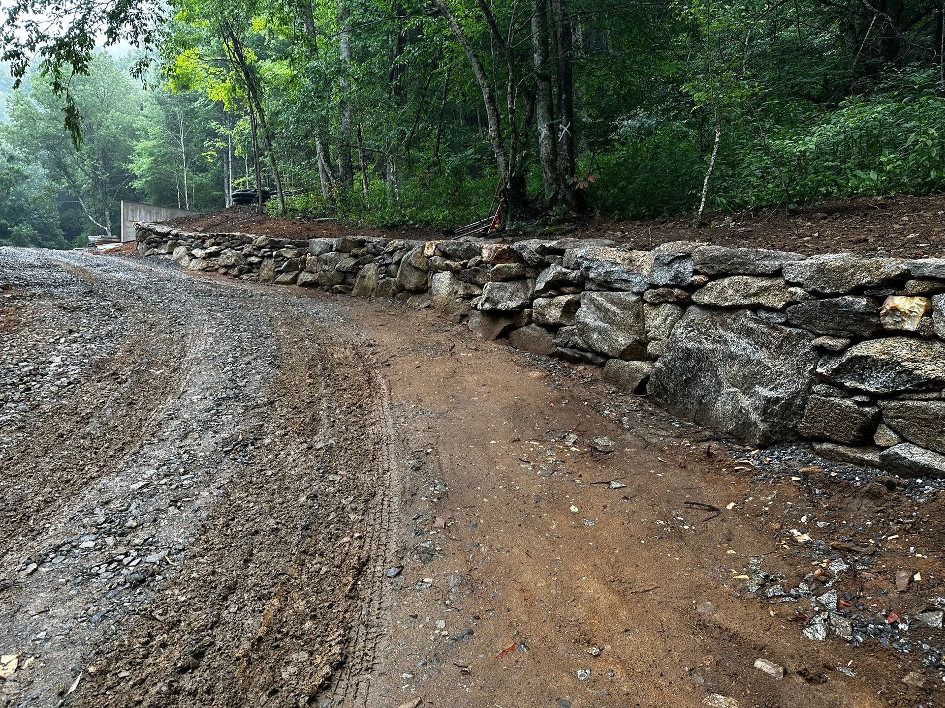 A dirt road with a stone wall on the side of it.