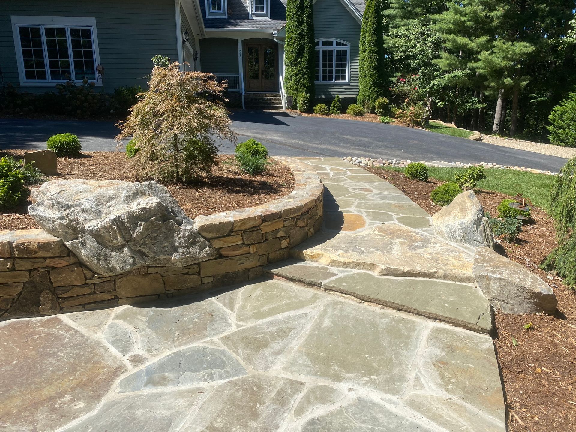 A stone walkway leading to a house with a large rock in the middle.